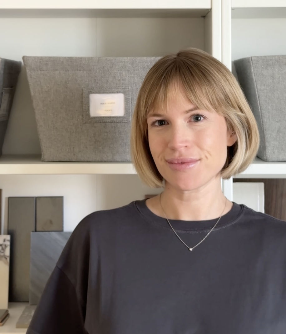 A woman with blonde hair and a black shirt standing in front of shelves with fabric sample boxes and tiles.