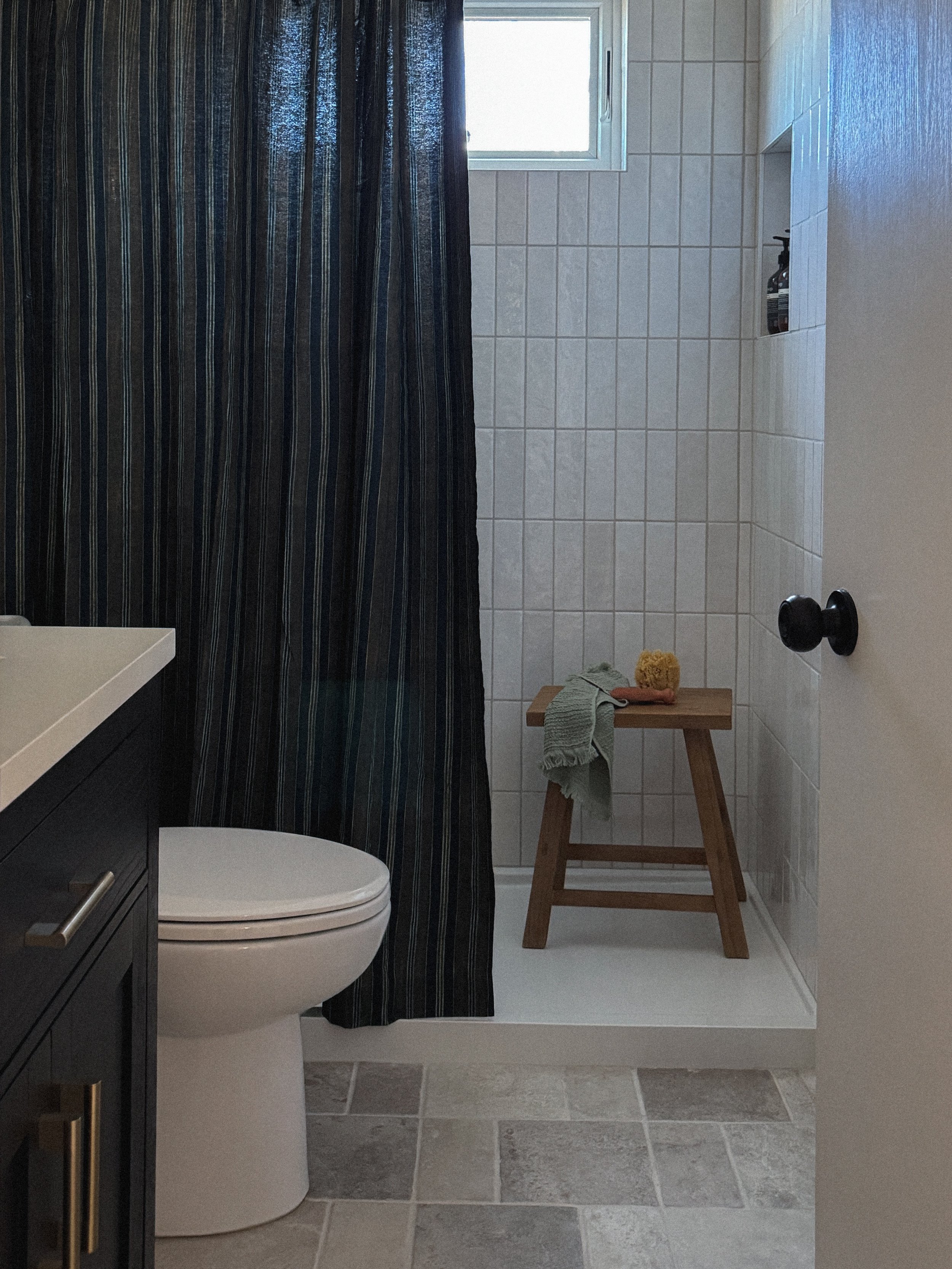 Modern mountain bathroom remodel with zeliege shower tile, wood stool, and tumbled limestone floors in Steamboat Springs, Colorado