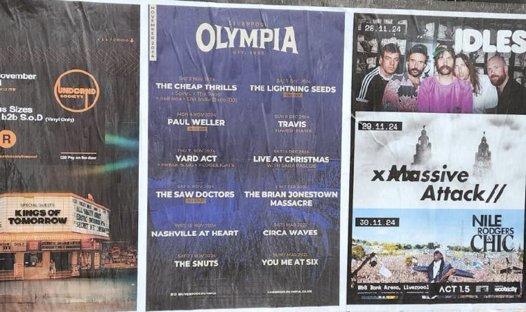 Three concert posters and a band poster on a wall featuring various bands and event dates.