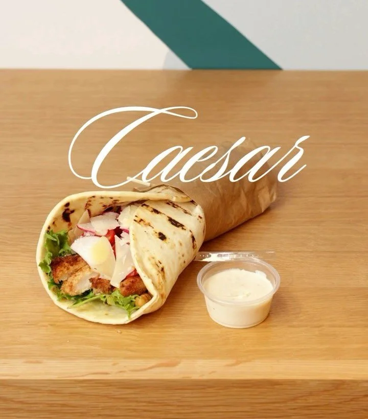 Radish Kitchen’s Caesar wrap placed on a wooden base with mayo on the side.