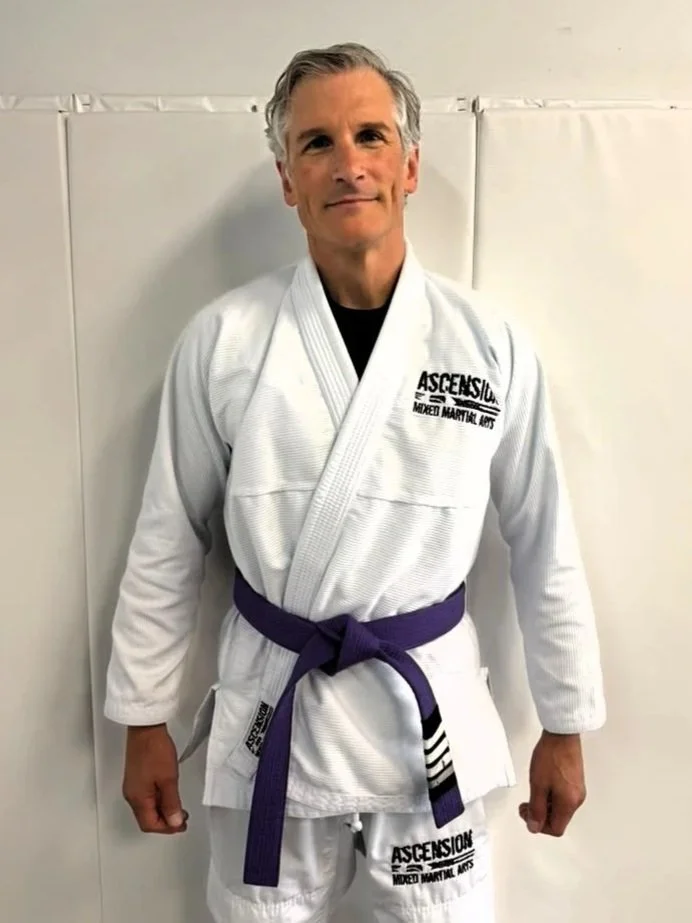 Man wearing a white Brazilian Jiu-Jitsu gi with blue belt and CTRL Industries logos