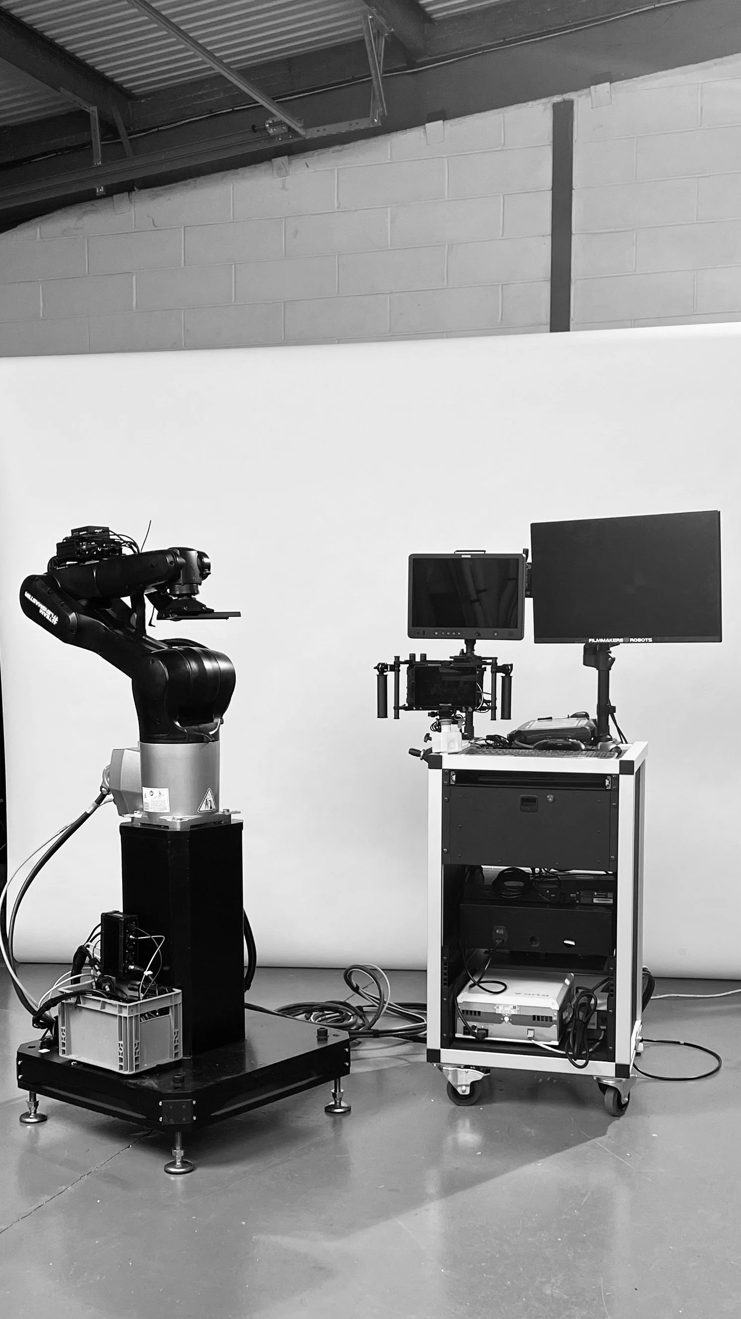 A robotic arm on a platform with cables connected, situated next to a mobile workstation with monitors and electronic equipment.