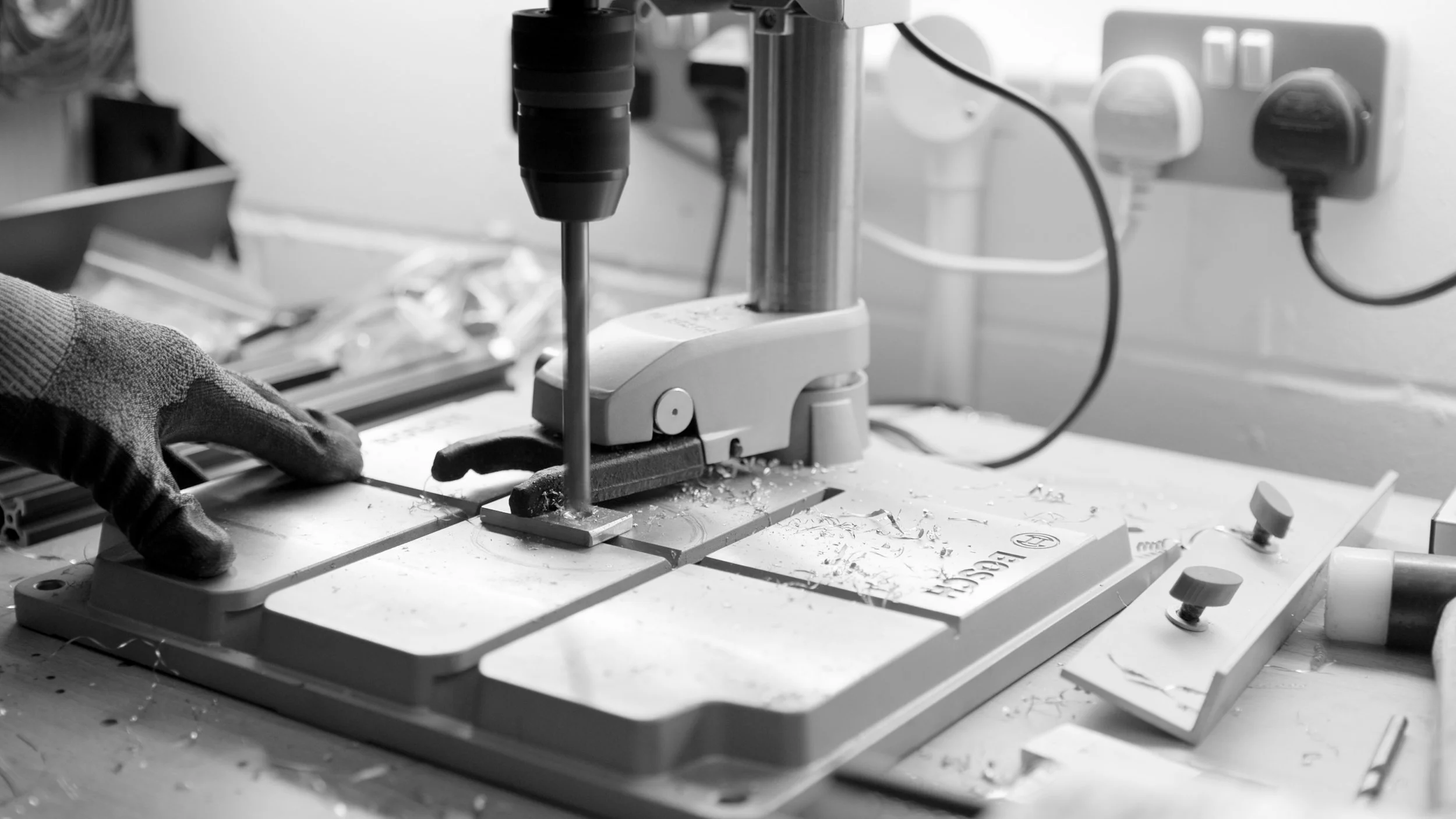 A person wearing gloves operating a bandsaw in a workshop, cutting a piece of material.