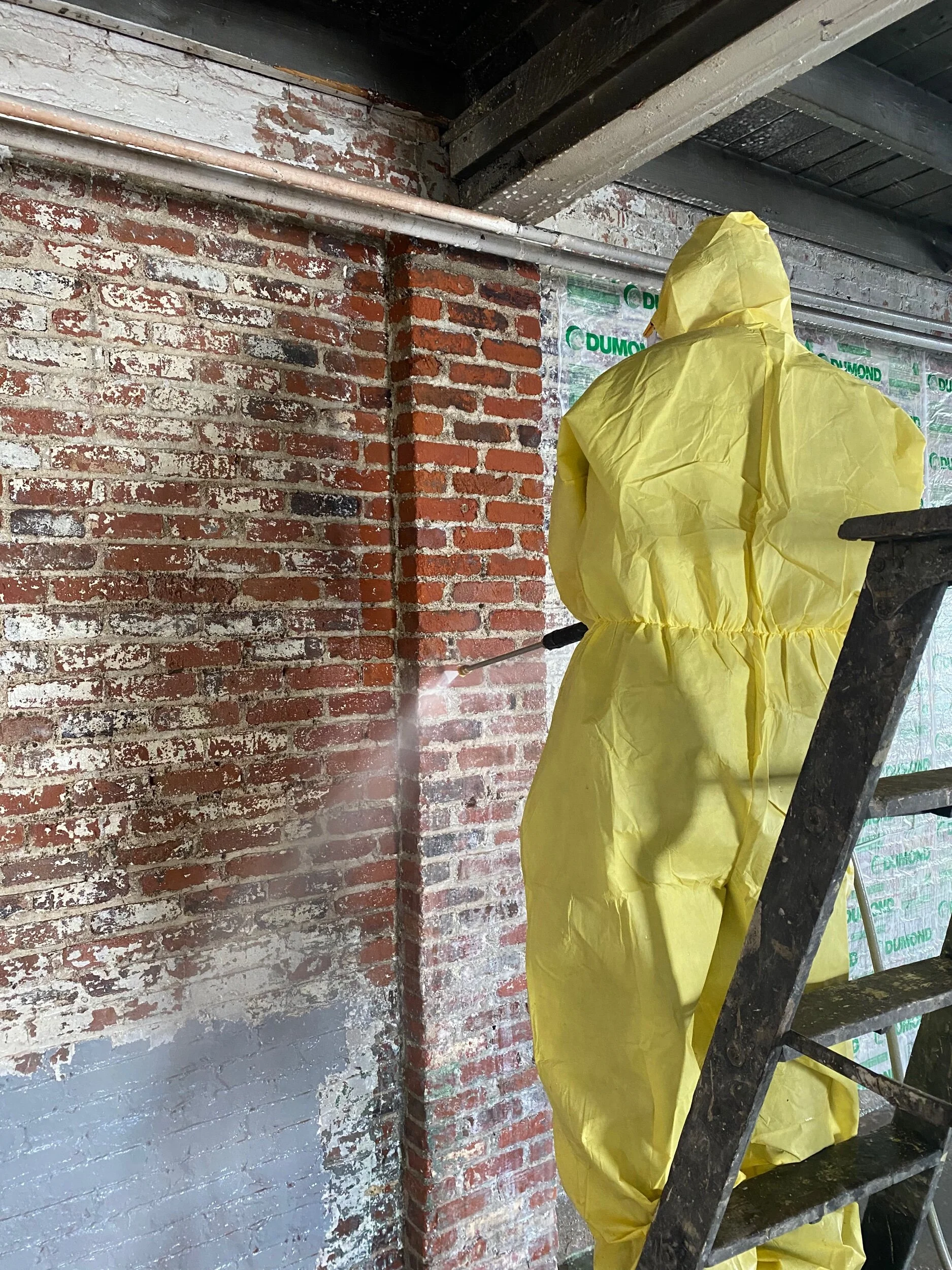 Stripping multiple layers of paint to expose the original brick beneath.