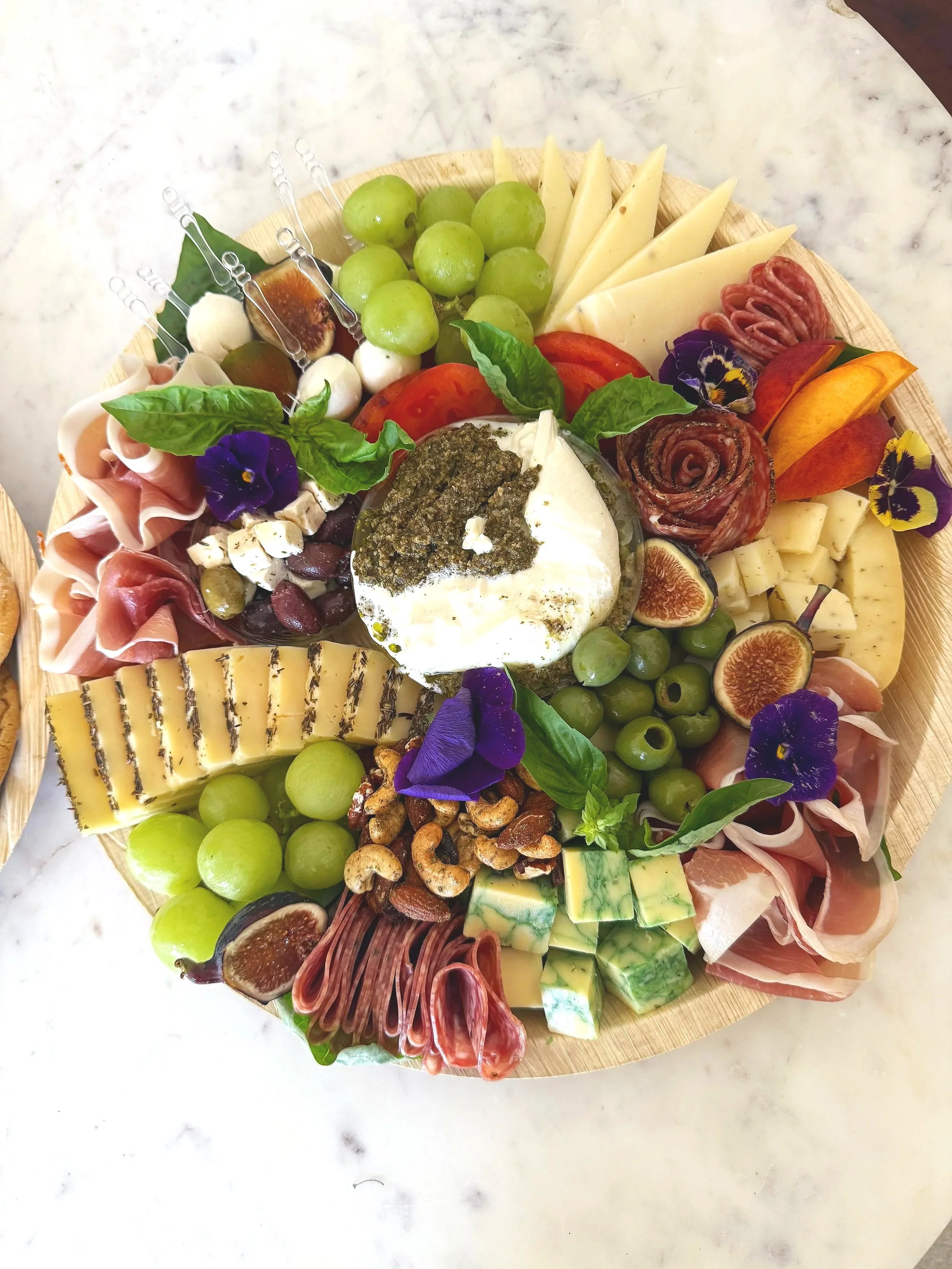 Assorted charcuterie board with cheese, grapes, figs, nuts, sliced meats, and edible flowers