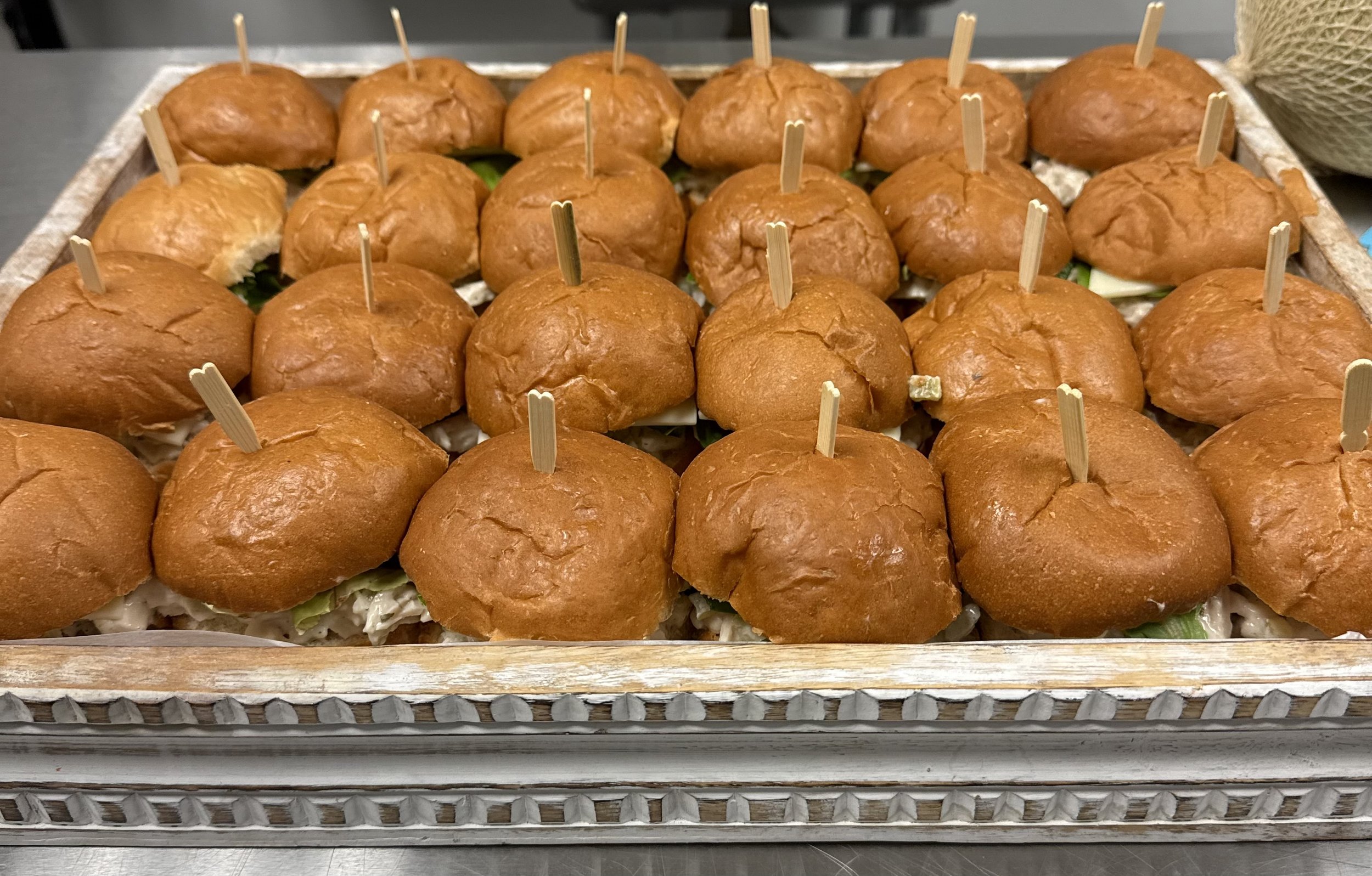 A tray of small slider sandwiches with hamburger buns and fillings, each with a toothpick.