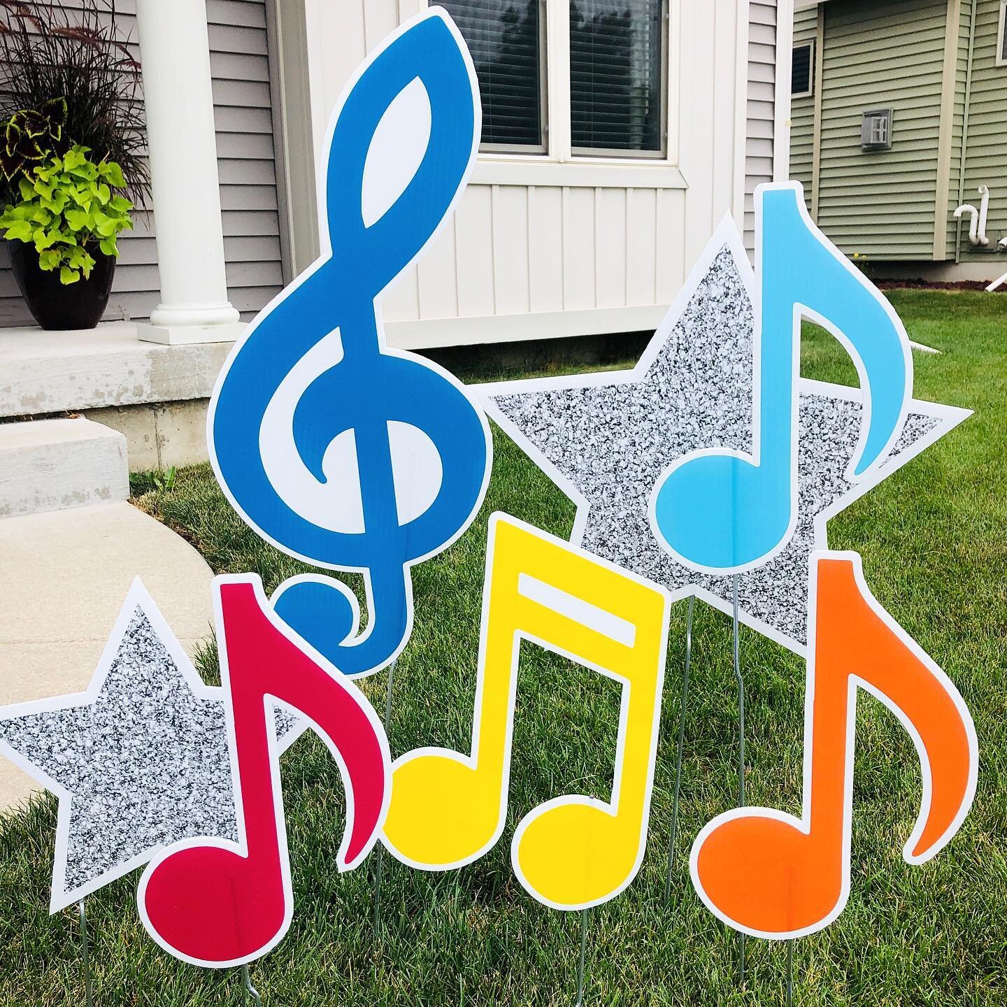 Colorful musical note yard signs with stars on a lawn in front of a house.