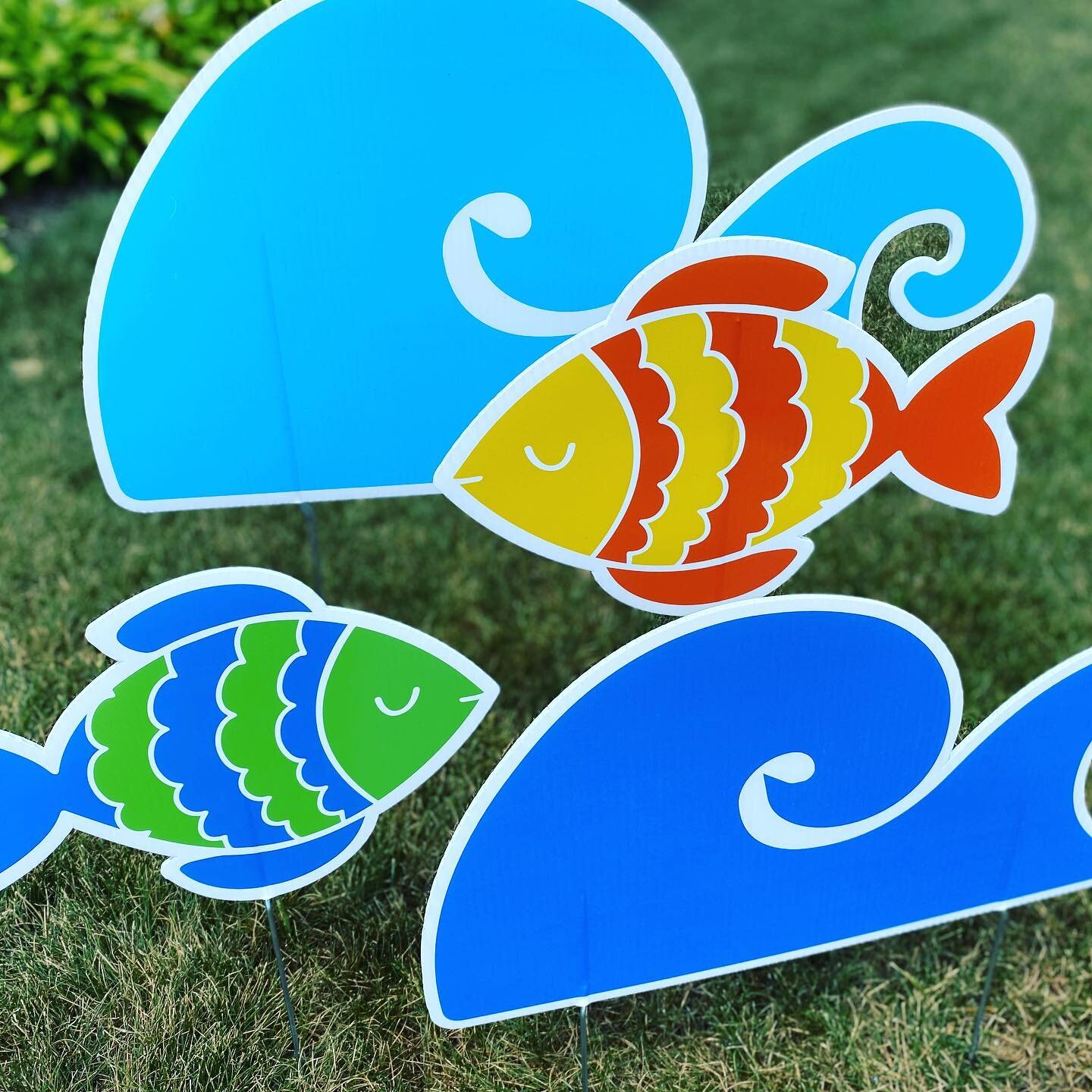 Colorful cartoon fish and wave signs on grass.