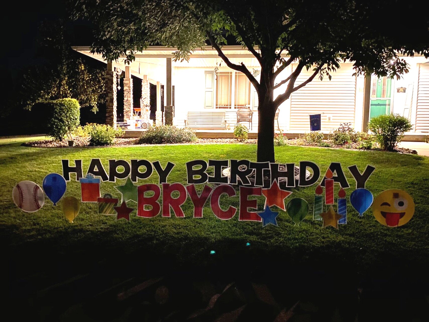 Outdoor 'Happy Birthday Bryce' sign with balloons and colorful decorations at night in front of a house.