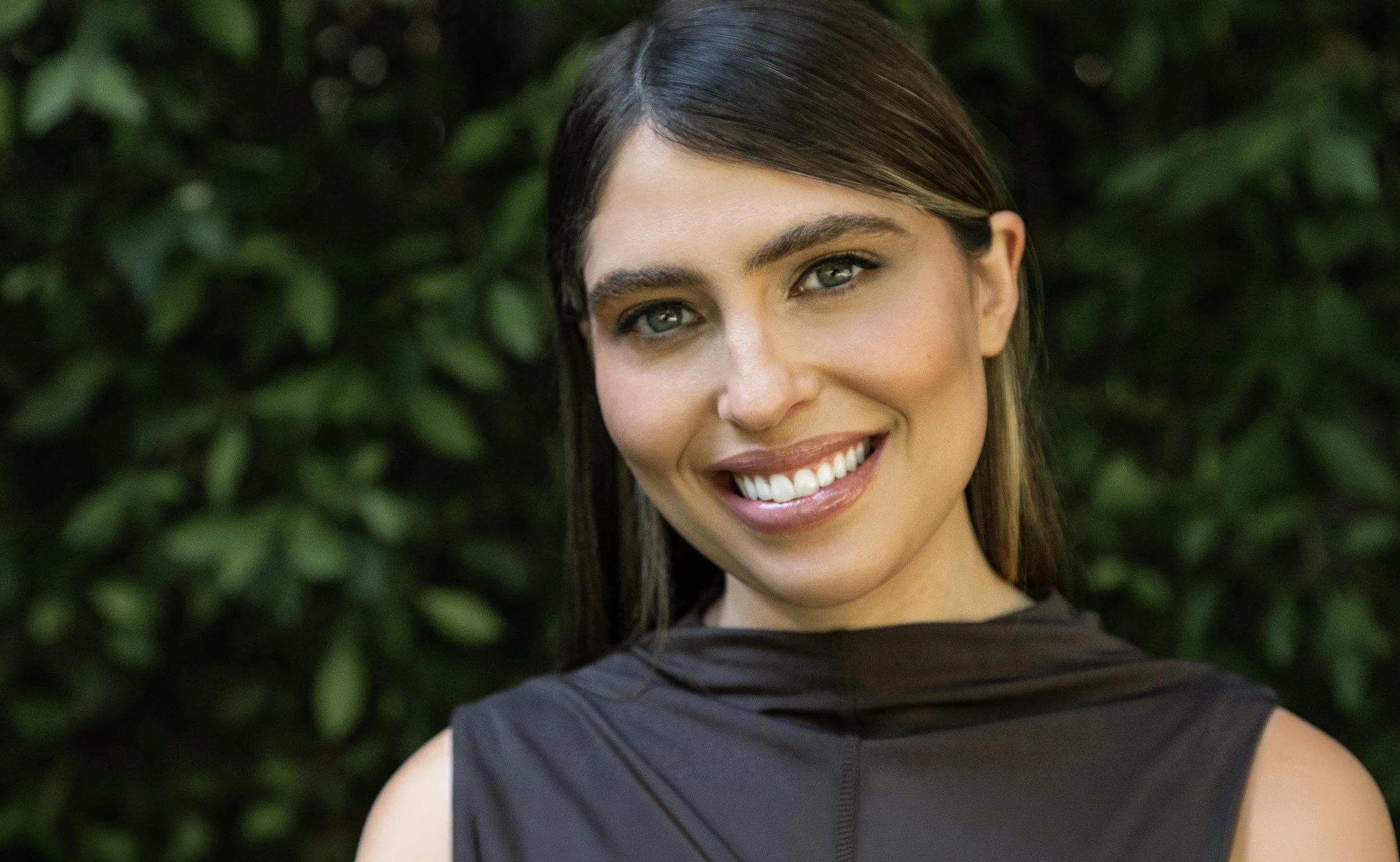 Close-up portrait of a woman with short dark hair, blue eyes, and light makeup, wearing a black blazer and a light blue shirt.