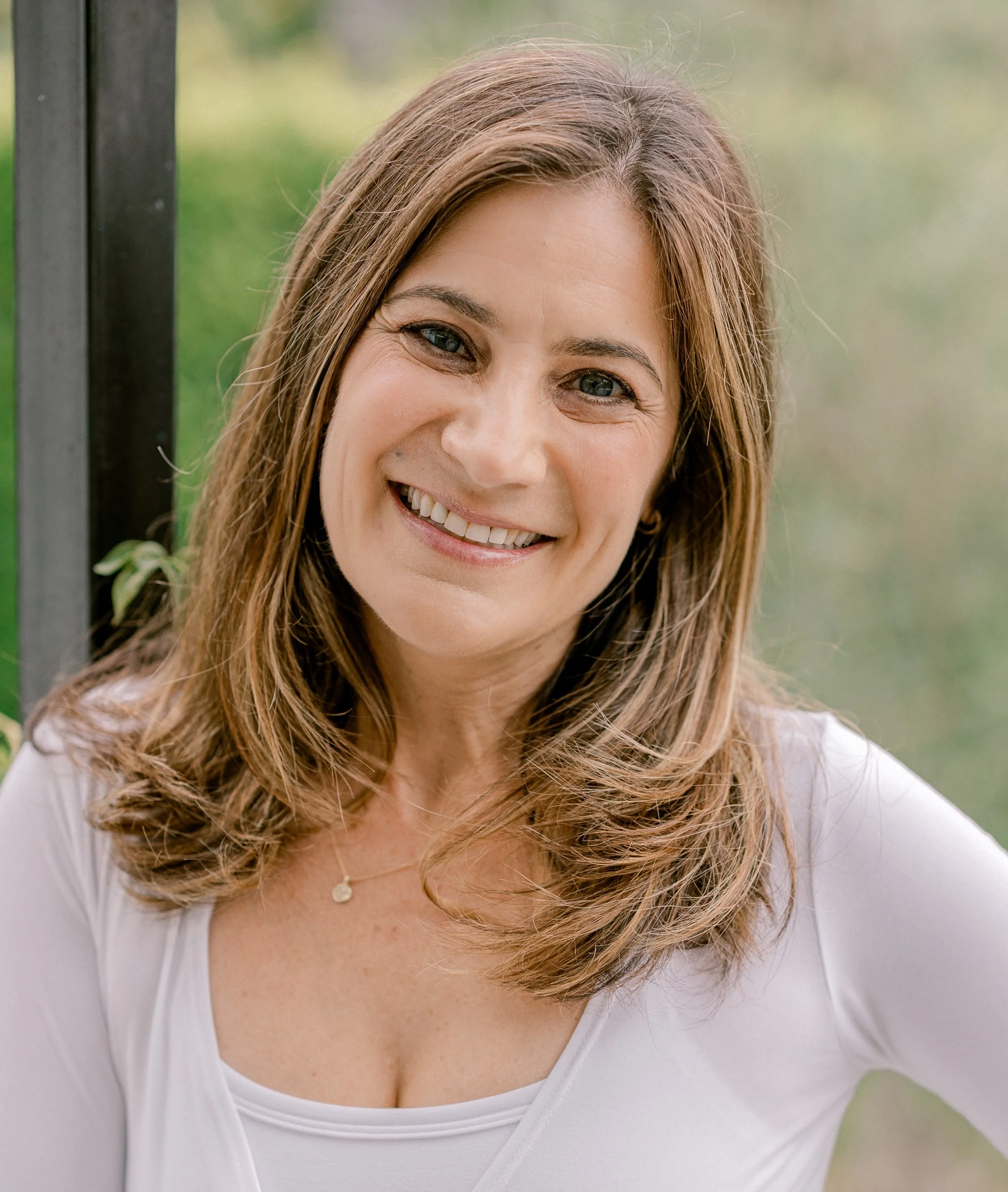 Liat Considine, C-IAYT, smiling outdoors in a white top
