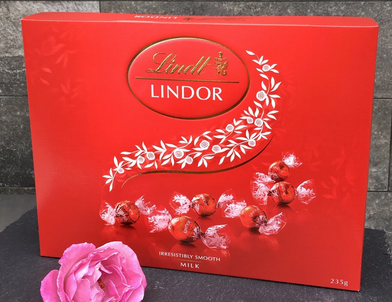 Red and delicious lindt milk chocolate box with pink flower in foreground (Copy)
