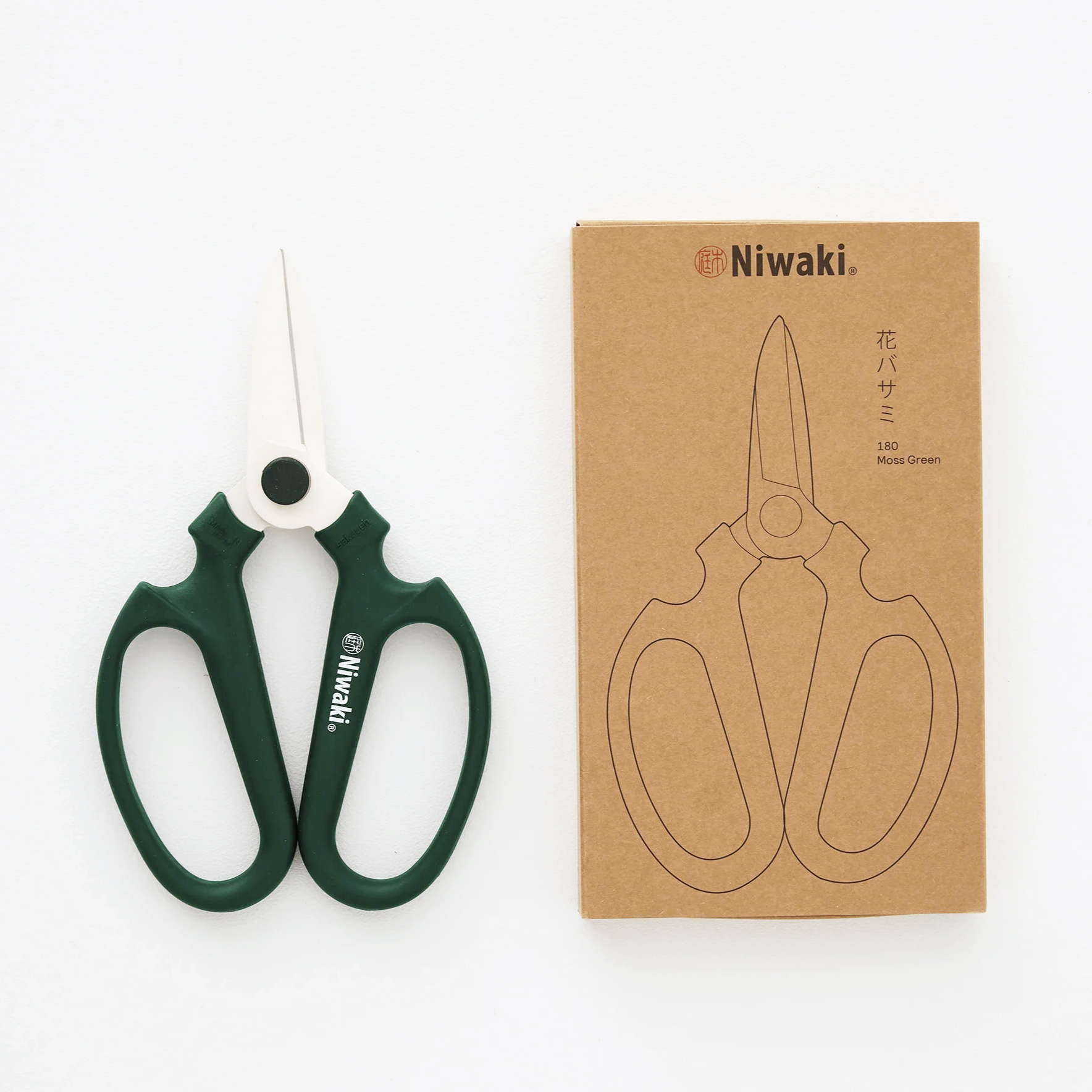 Forbici da potatura Niwaki di colore verde — utensili professionali per giardinaggio e floricoltura con impugnature ergonomiche e packaging di cartone con forma di forbici, sull'etichetta è scritto 'Niwaki' '180 Moss Green'