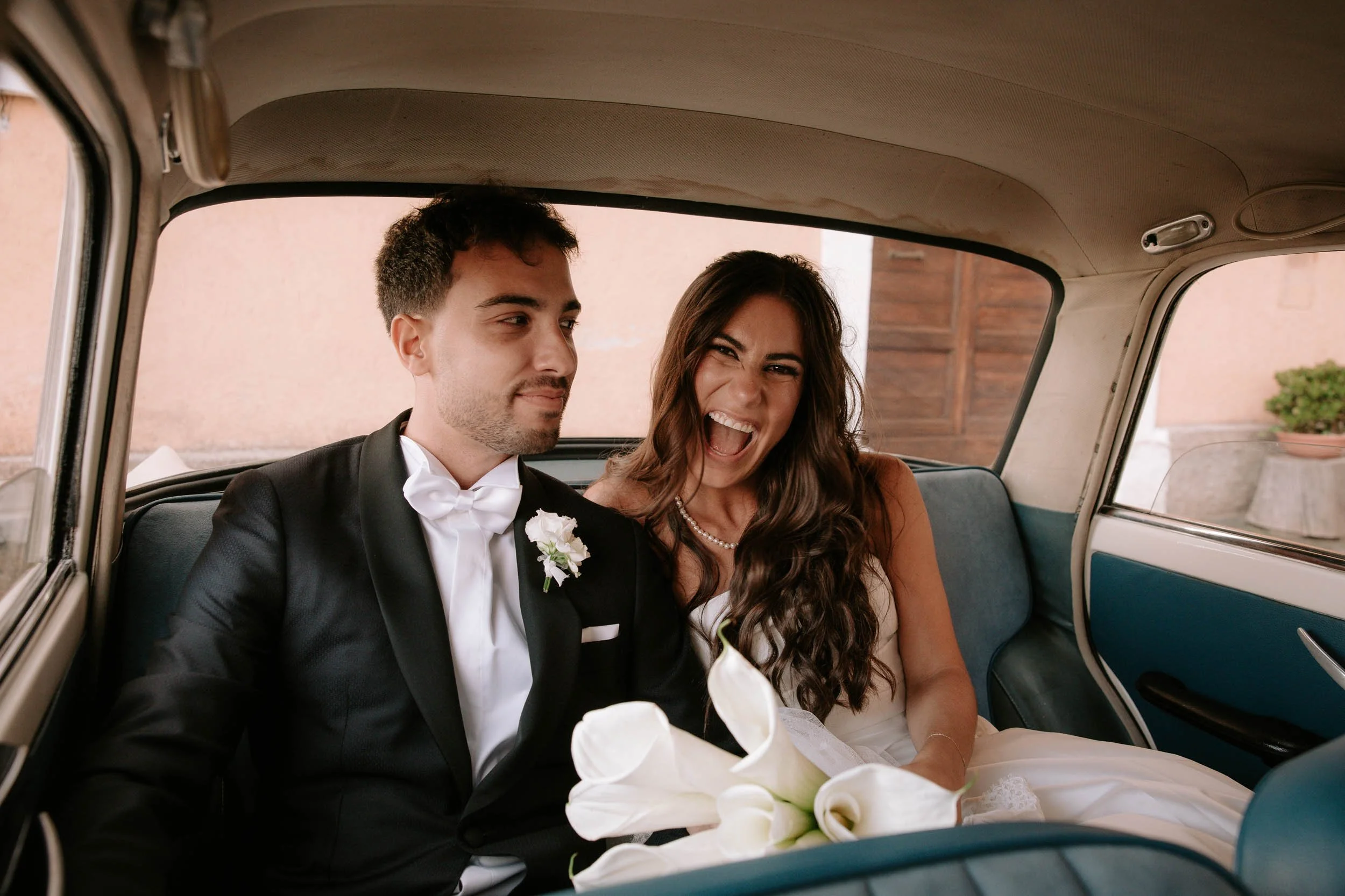 a happy couple, newly married, smile and laugh in the car taking them from the ceremony to reception.