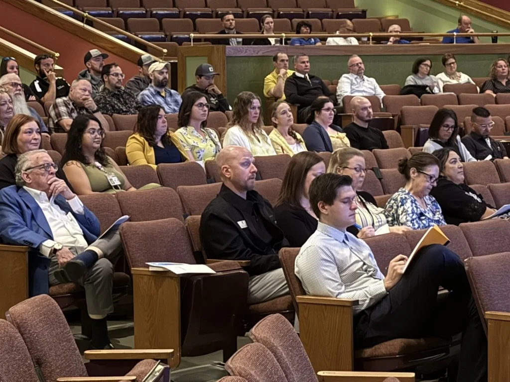 Audience seated in a theater or conference hall, watching a presentation or speech.