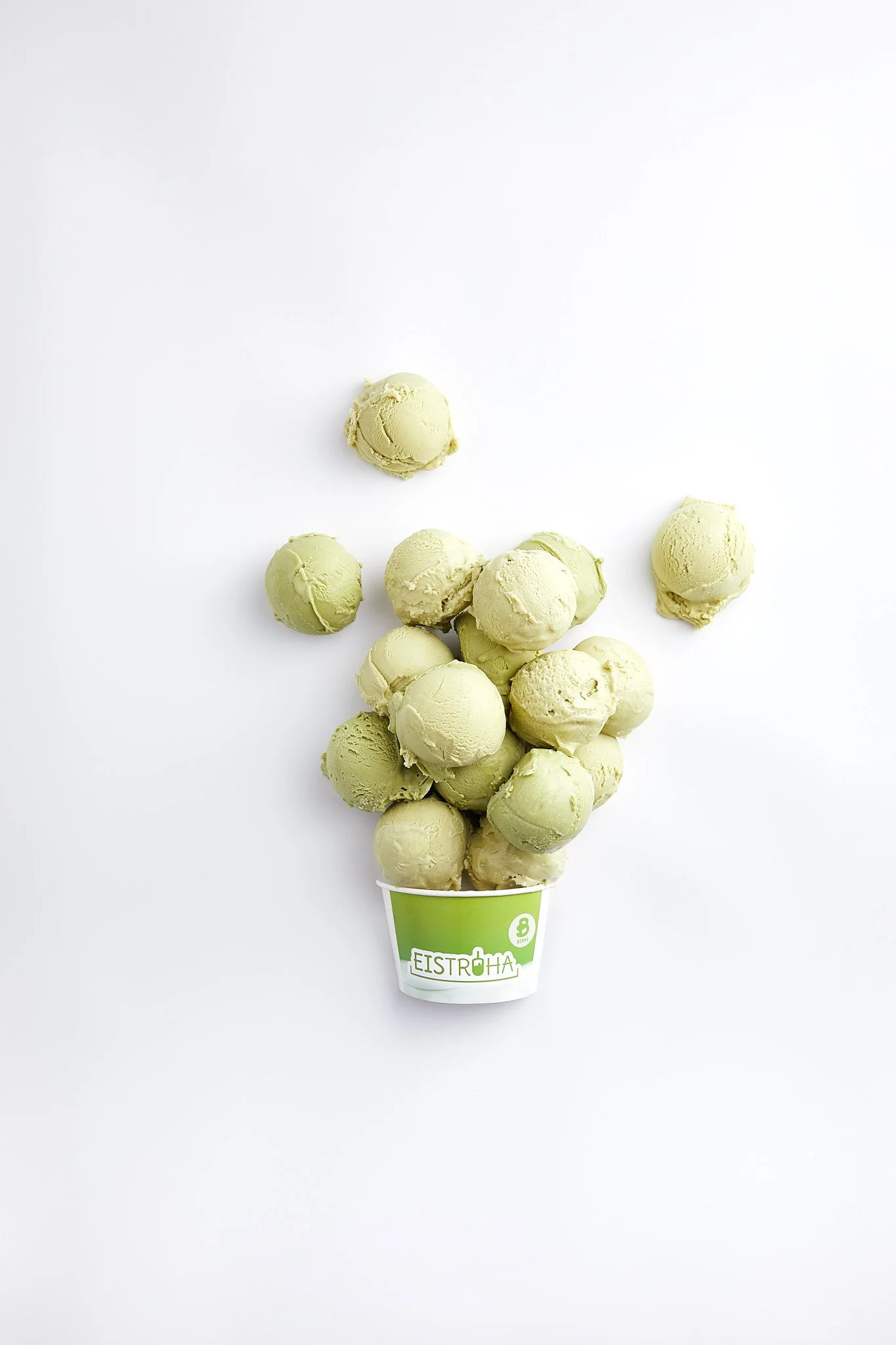 Gruppierung von grünen Kugeln in einem grünen Becher mit dem Aufdruck Eistroha auf einem weißen Hintergrund. Fotografiert von Sarah Neuner.