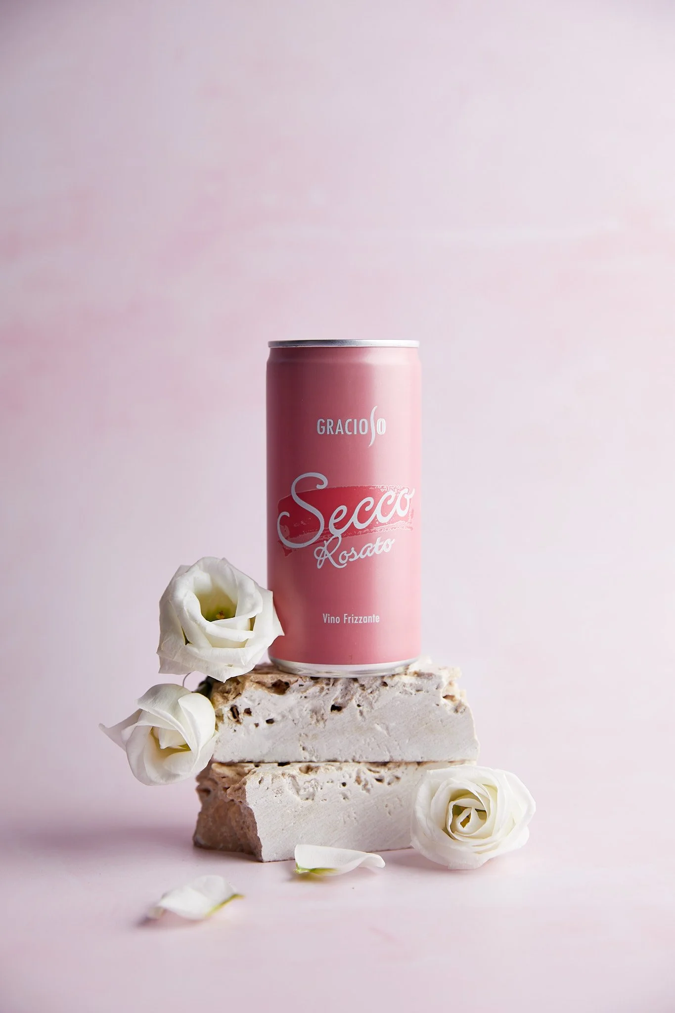 Eine Dose Secco Rosato auf einer Marmorplatte, umgeben von weißen Rosenblüten auf hellem pinkem Hintergrund. Fotografiert von Sarah Neuner.
