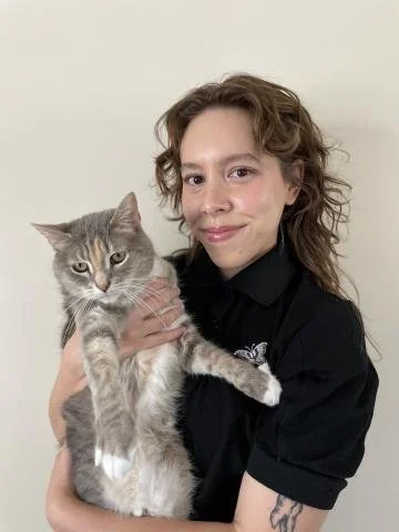 woman with brown curly hair in a black turtle neck holding a grey and white cat