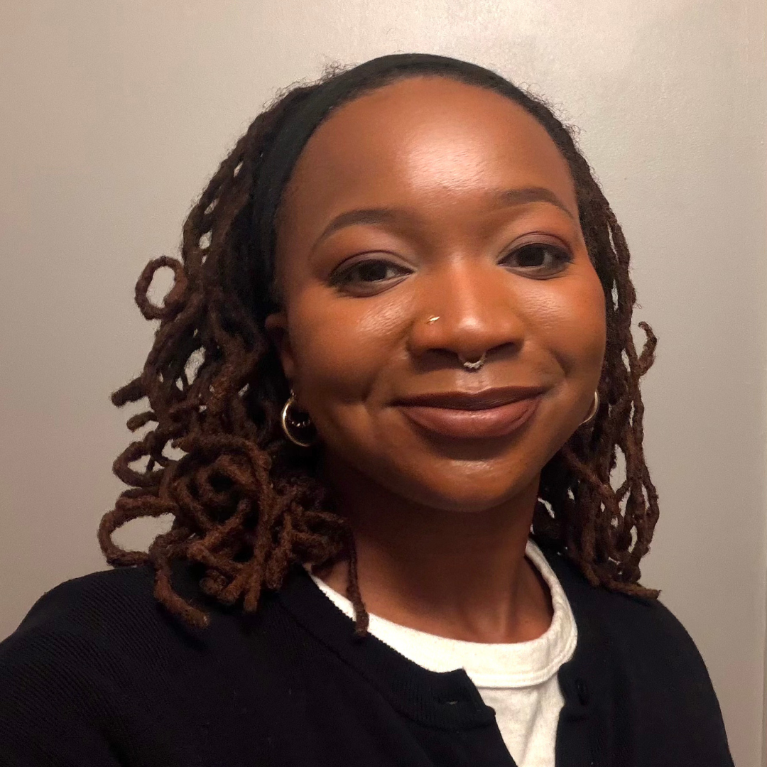 Woman with brown curly braids and a white shjirt under a black v-neck