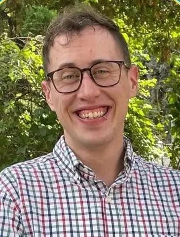 Man with short brown hair, glasses, and a lip ring, smiling 