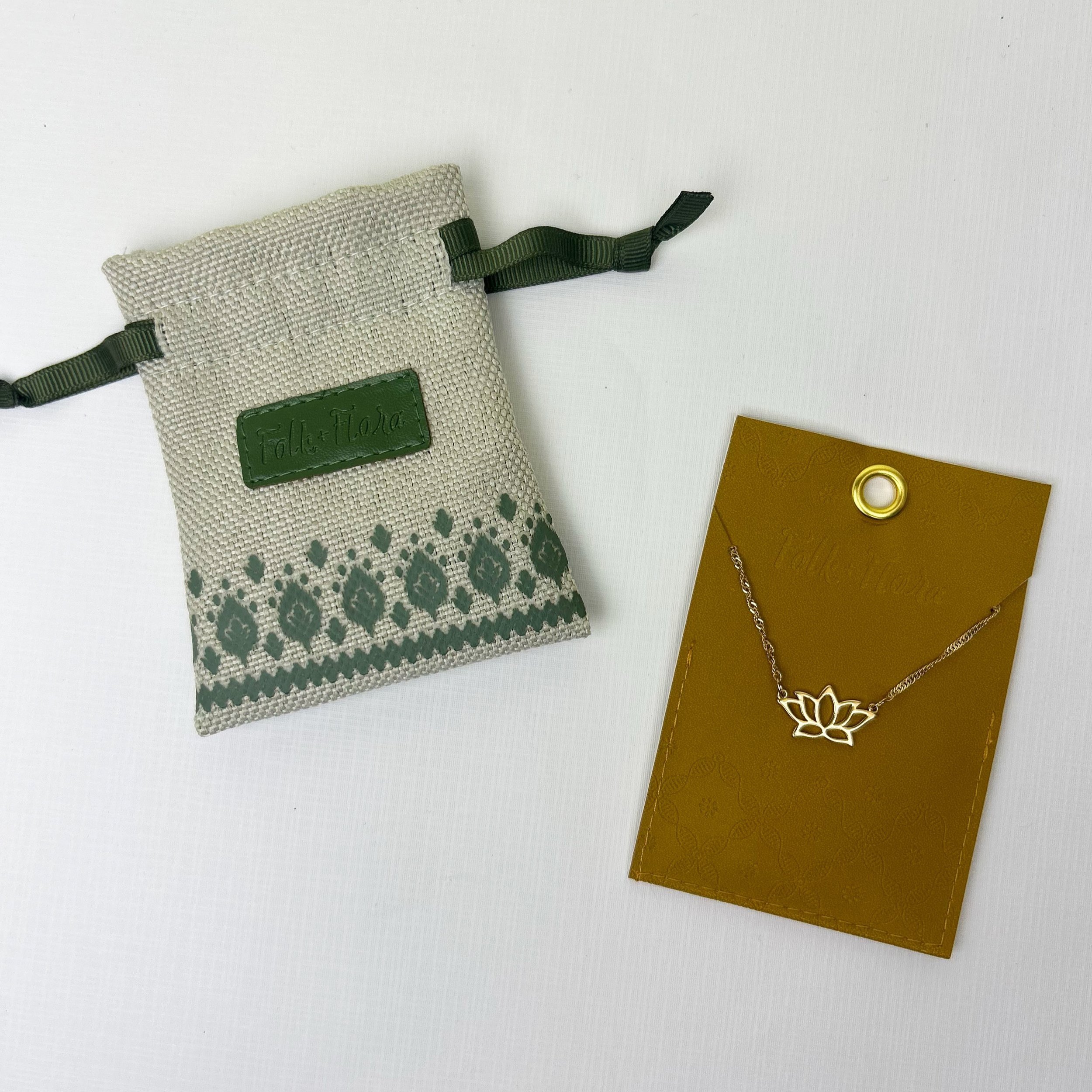 Jewelry pouch with green trim and drawstrings next to a gold-colored necklace with a lotus pendant on a mustard yellow card.