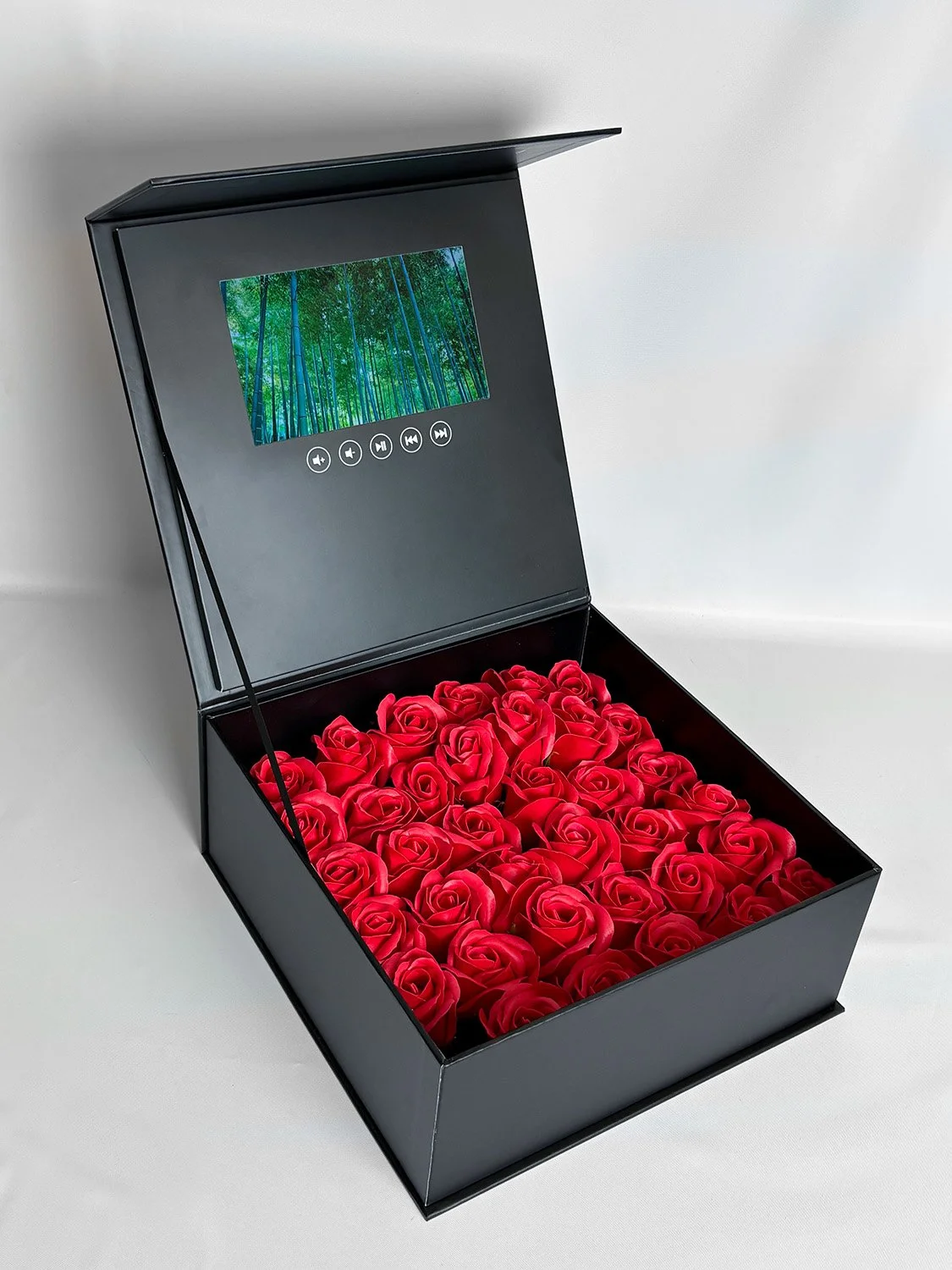 A black box with a lid that is opened, revealing red roses inside. The inside of the lid has a digital screen showing a forest scene and control buttons below it. influencer boxes A&H packaging video boxes