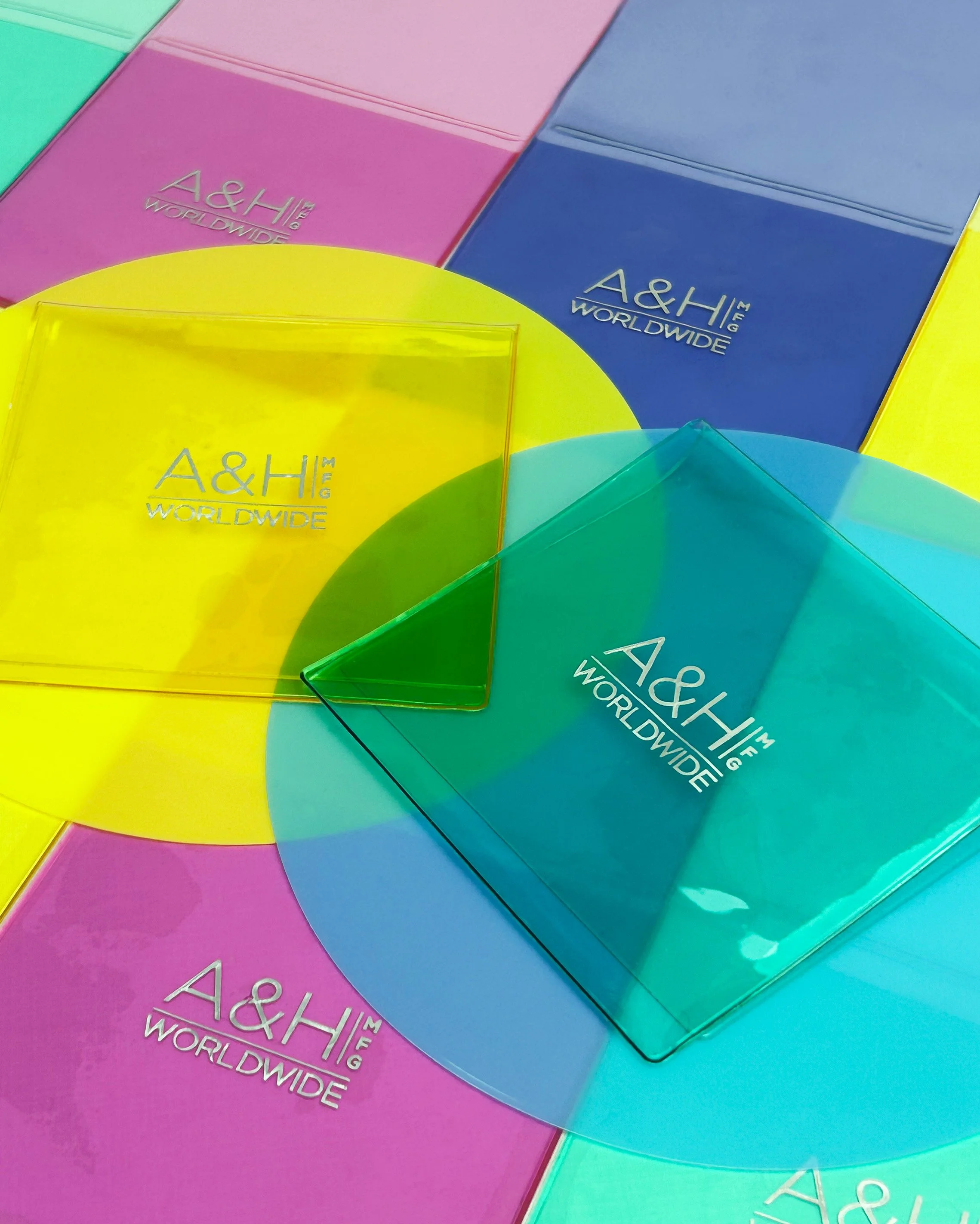Colorful A&H Worldwide stationery folders in pink, blue, yellow, and green with transparent corner protectors.