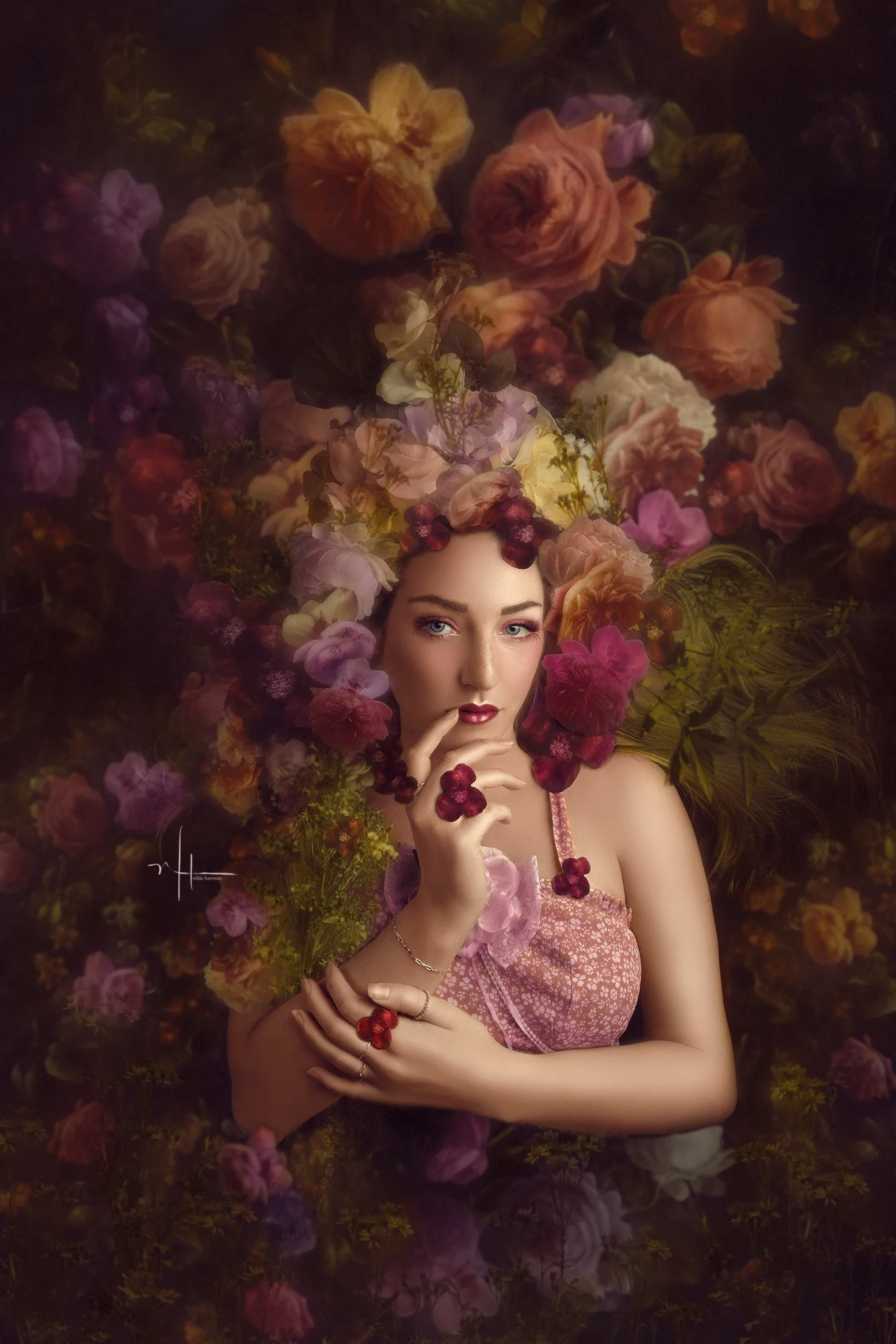 A woman with blue eyes and red lipstick, wearing a pink dress, surrounded by various flowers. Her hair is decorated with flowers, and she is touching her lips with her right hand while the left hand is placed on her right arm.