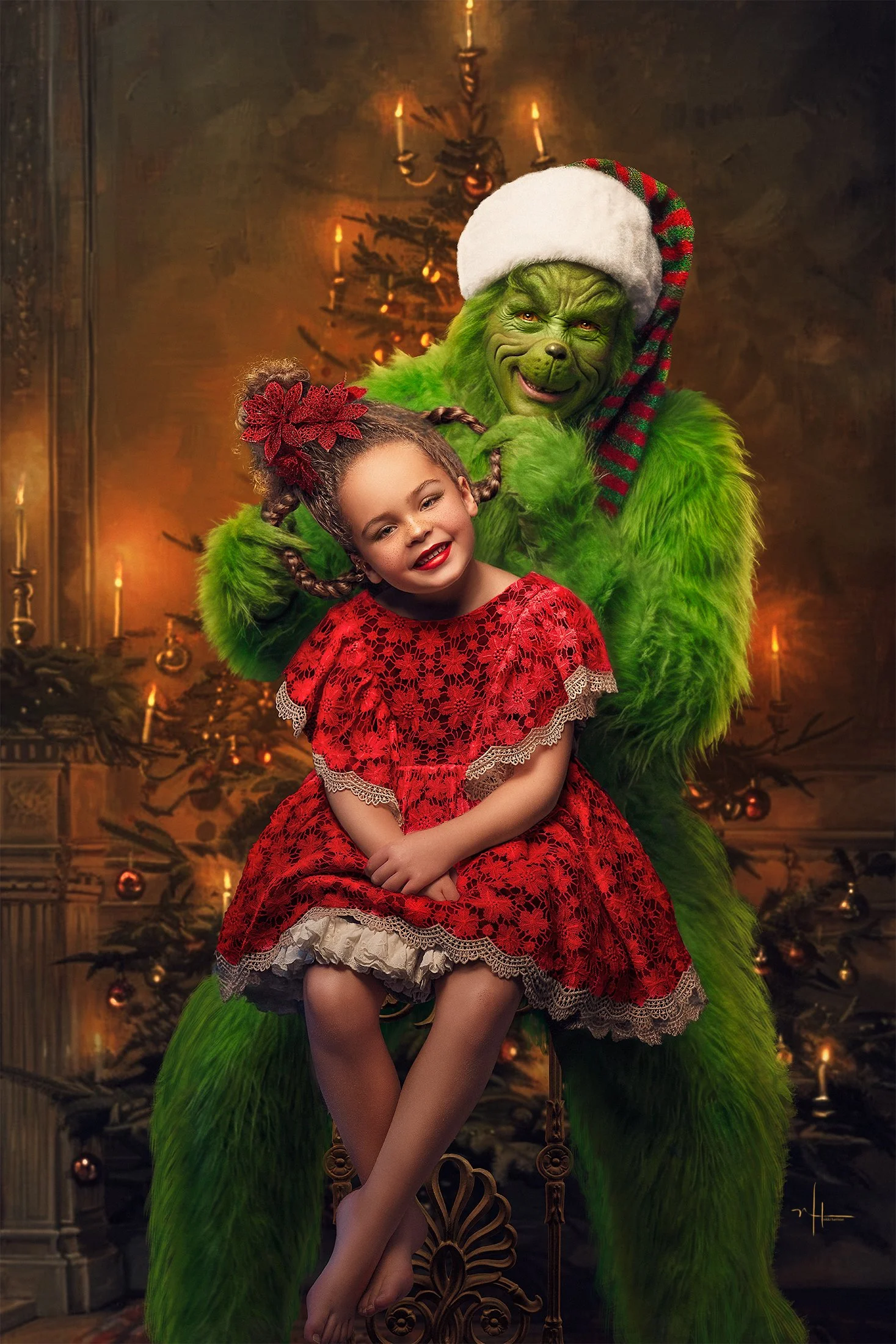 A young girl with curly hair, wearing a red lace dress, sitting on a decorative wooden chair, smiling with her eyes closed, in front of a decorated Christmas tree with candles and ornaments, with a large green Grinch figure behind her wearing a Santa
