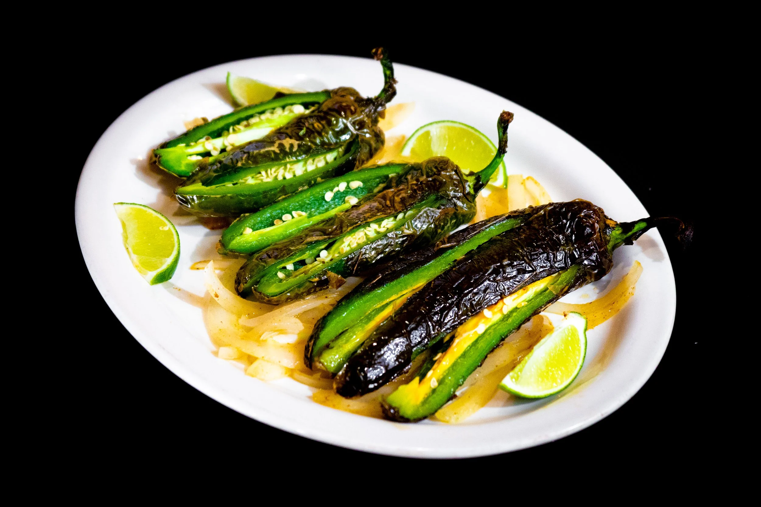 Plate of grilled jalapeño peppers garnished with lime wedges on a black background
