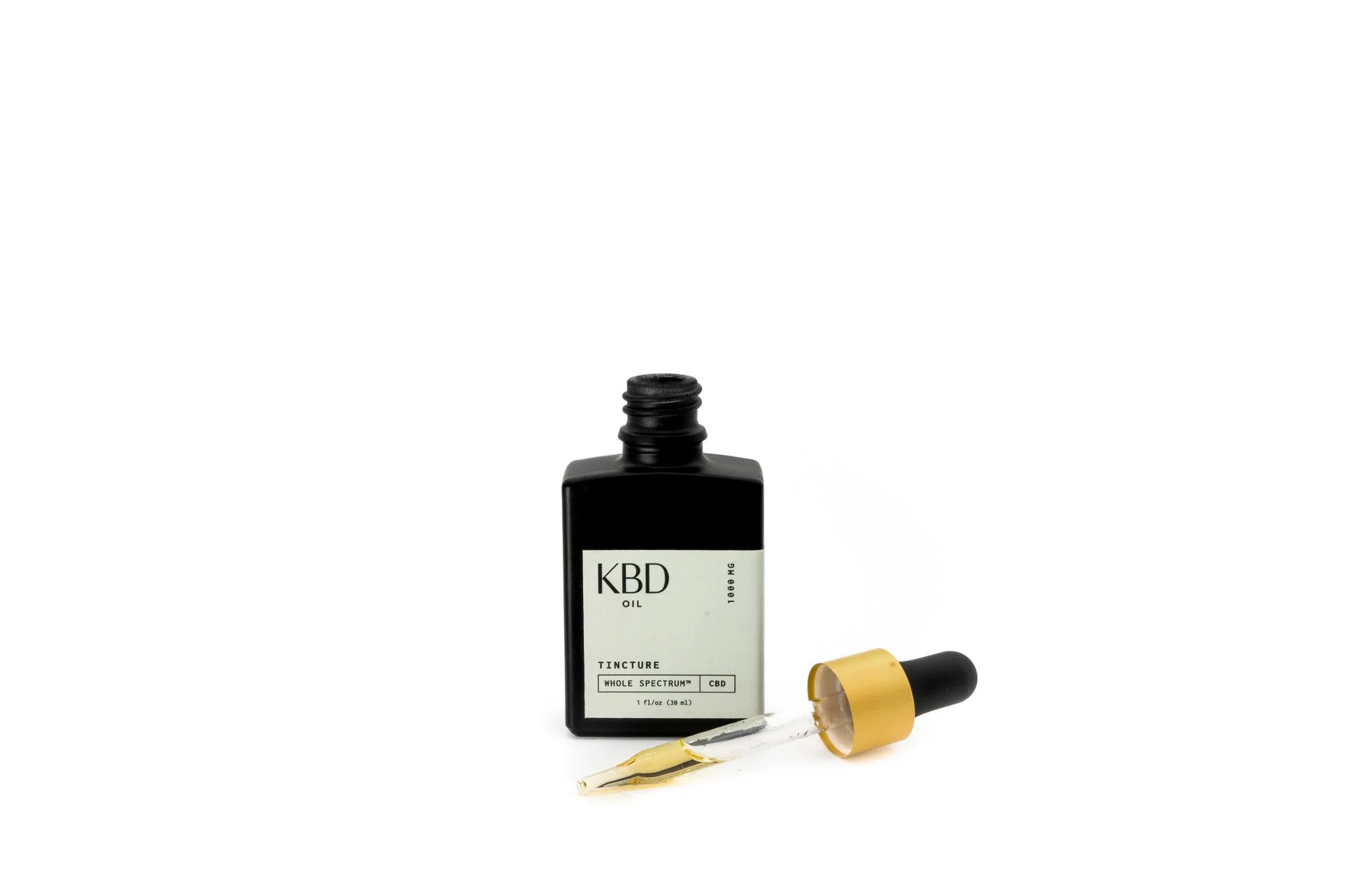 A black bottle of CBD oil with a label reading 'KBD Oil, Tincture, Whole Spectrum, CBD,' next to a glass dropper with a yellow cap, filled with CBD oil.