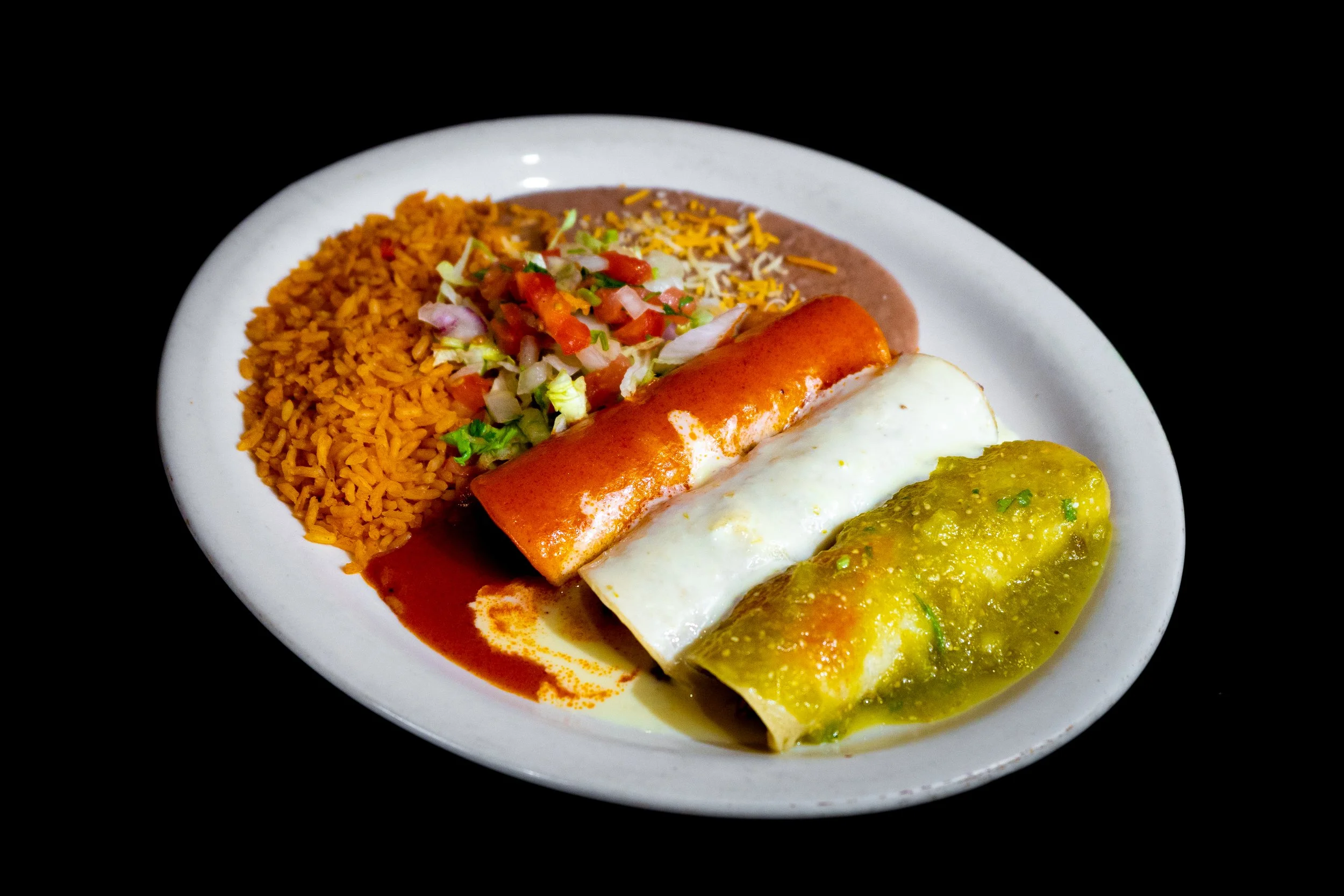 Plate of Mexican food including rice, salad, refried beans, a rolled taco, a cheese enchilada, and a green chile relleno, on a black background.