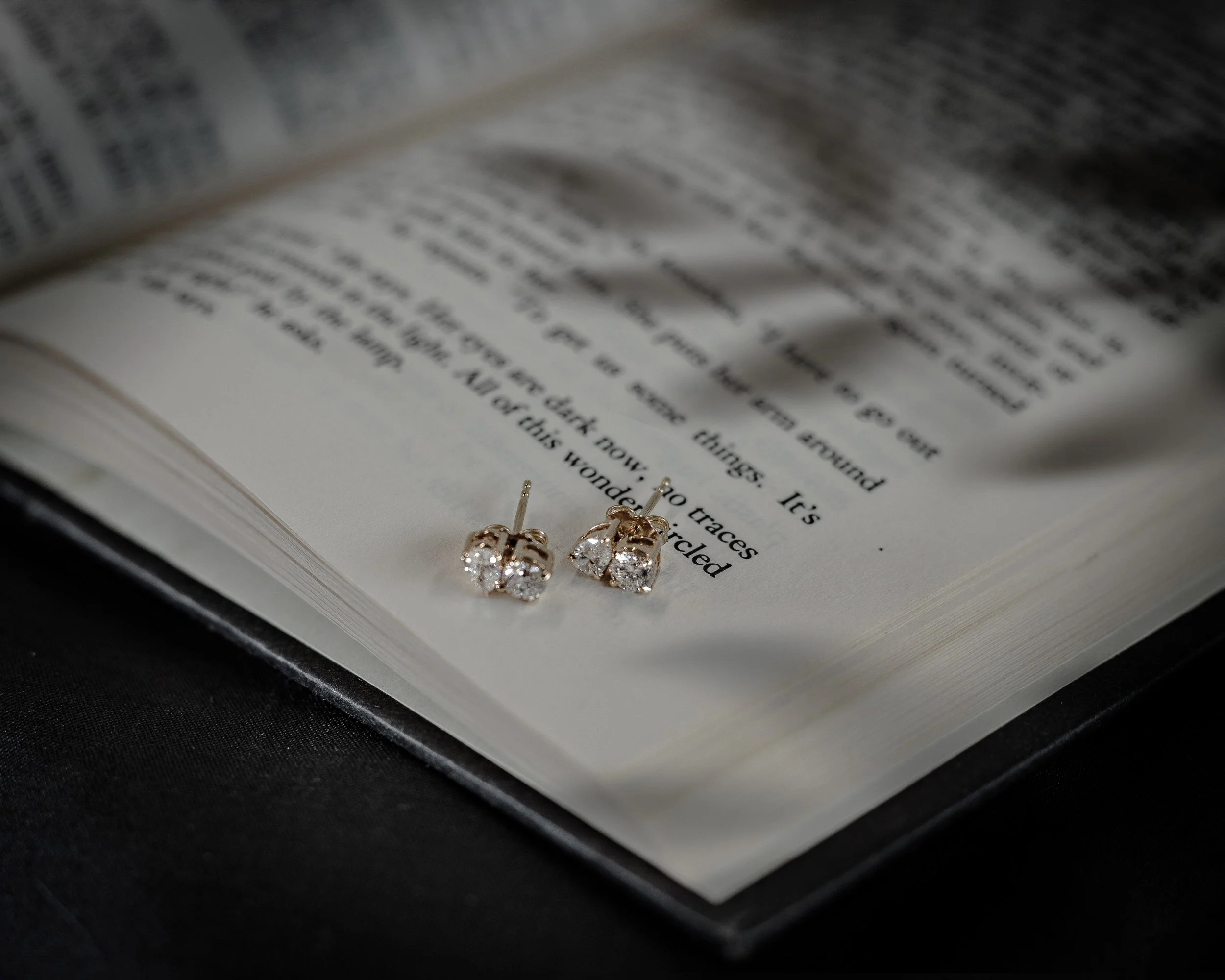 Close-up of diamond earrings on an open book with black background.