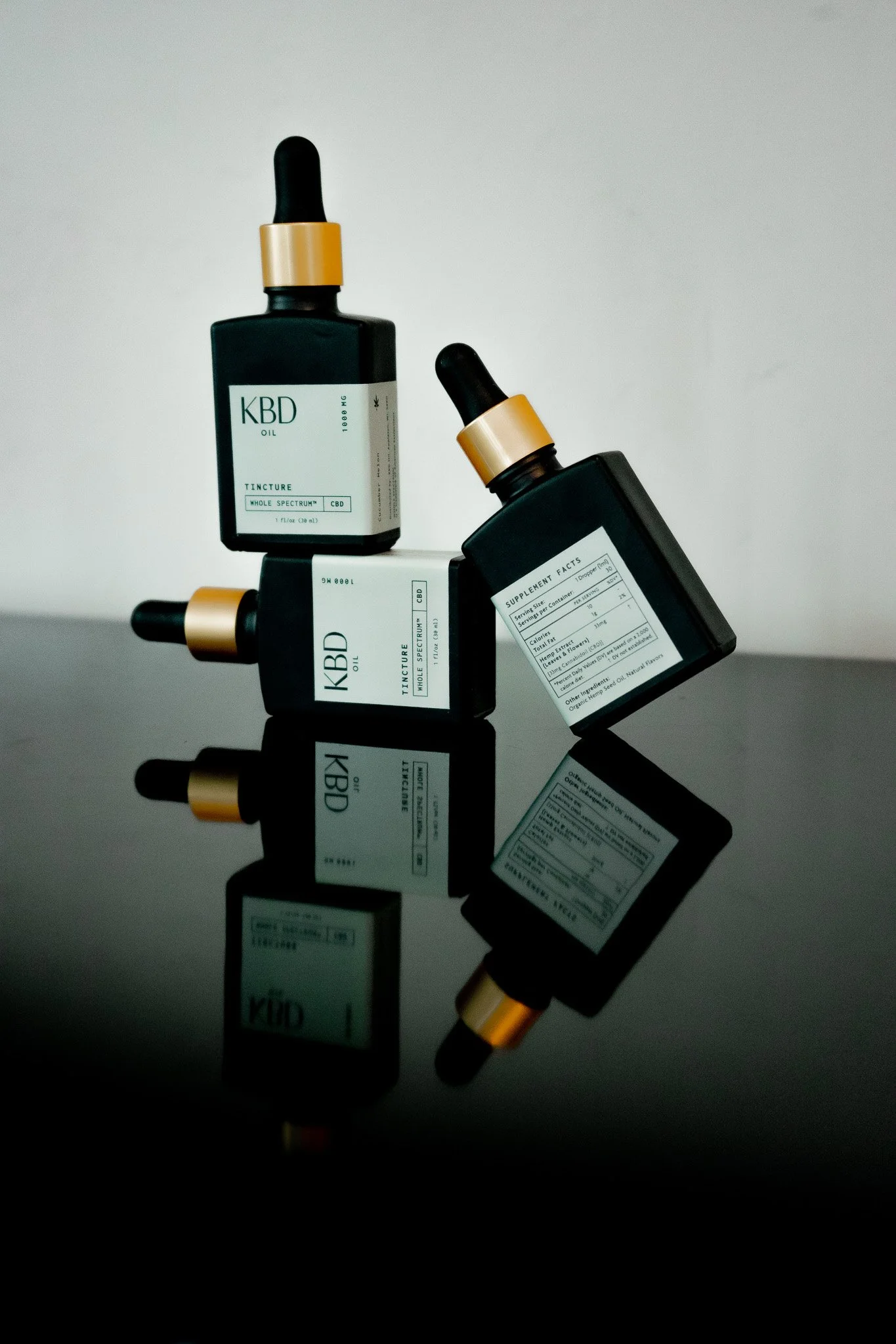 Three black bottles with gold caps labeled CBD oil, positioned on a reflective black surface, with their reflections visible.