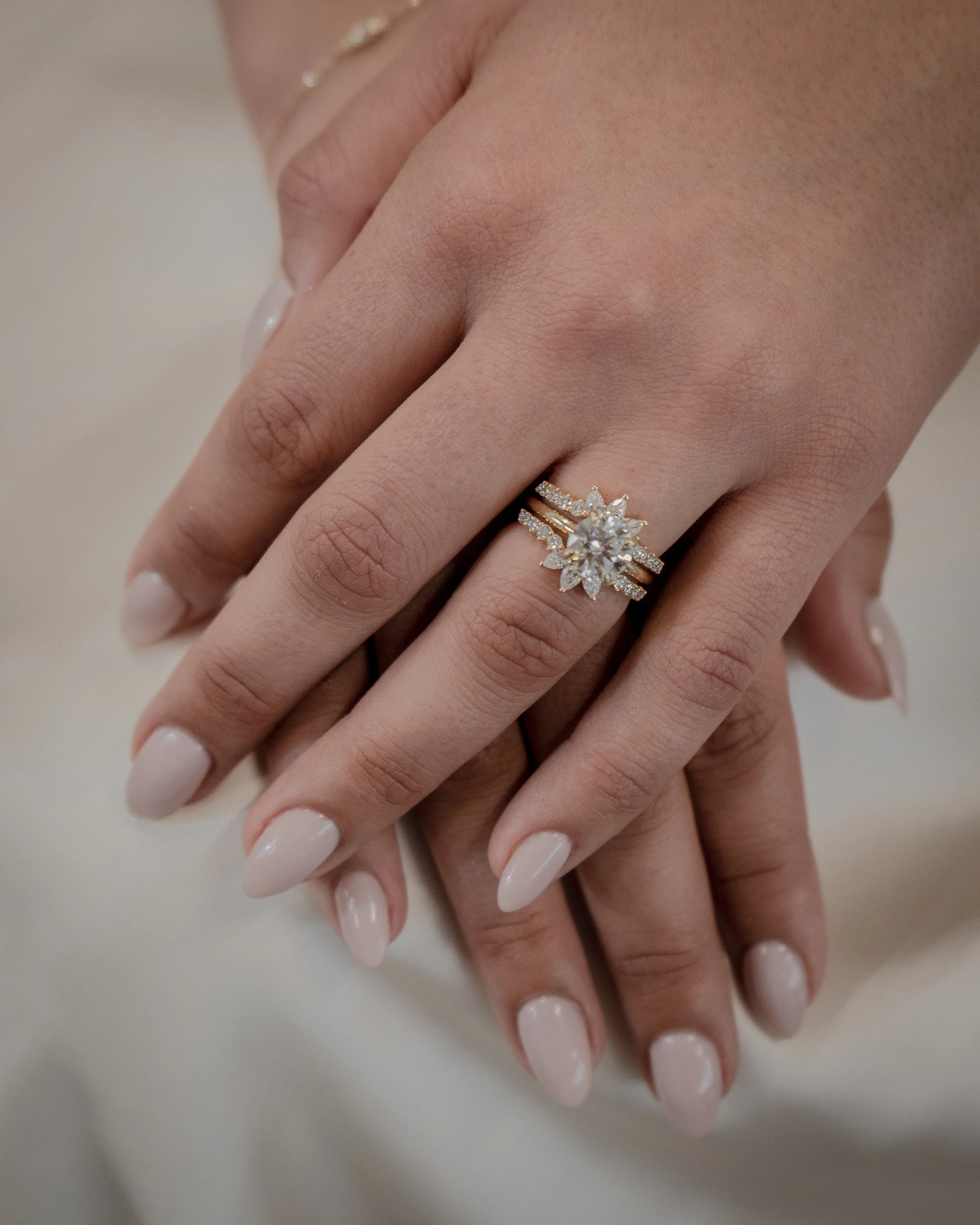 Hands with a wedding and engagement ring, featuring a large floral diamond centerpiece, on woman's finger, with polished nails.