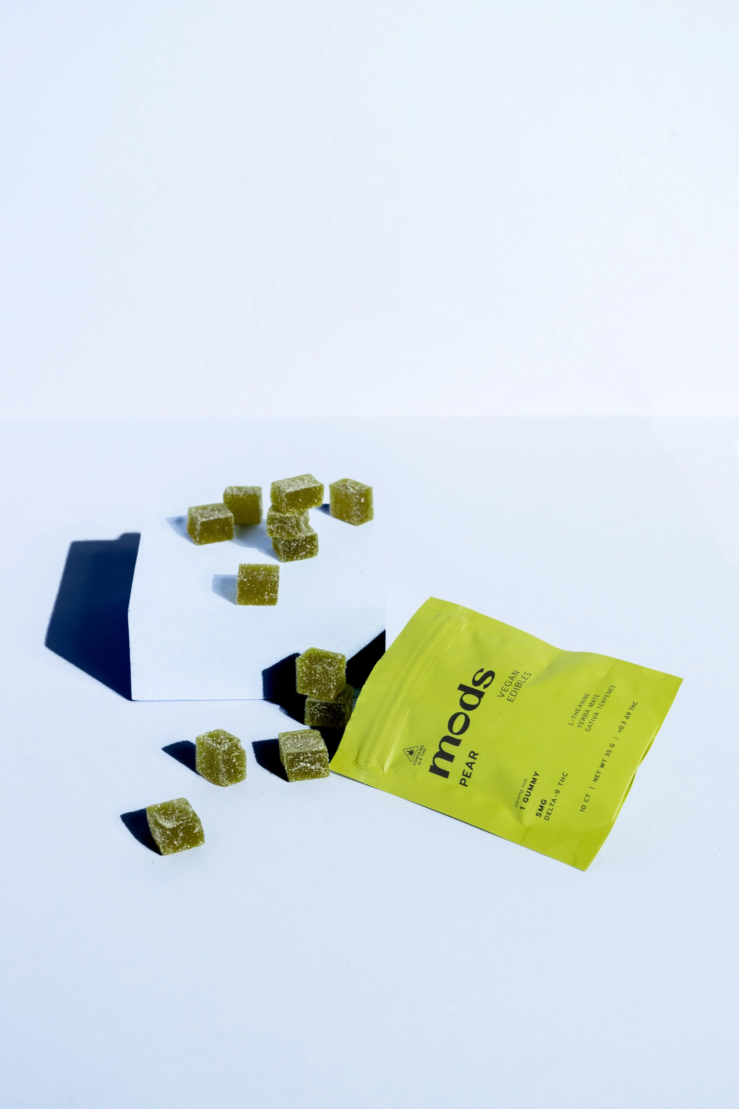 Green pear-flavored gummy candies on a white surface with a yellow packaging and a small white platform.