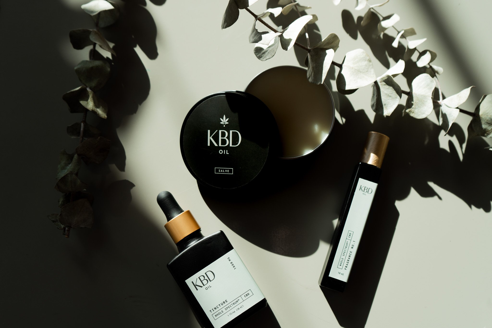 CBD oil products and a cannabis leaf with shadows cast on a white surface.
