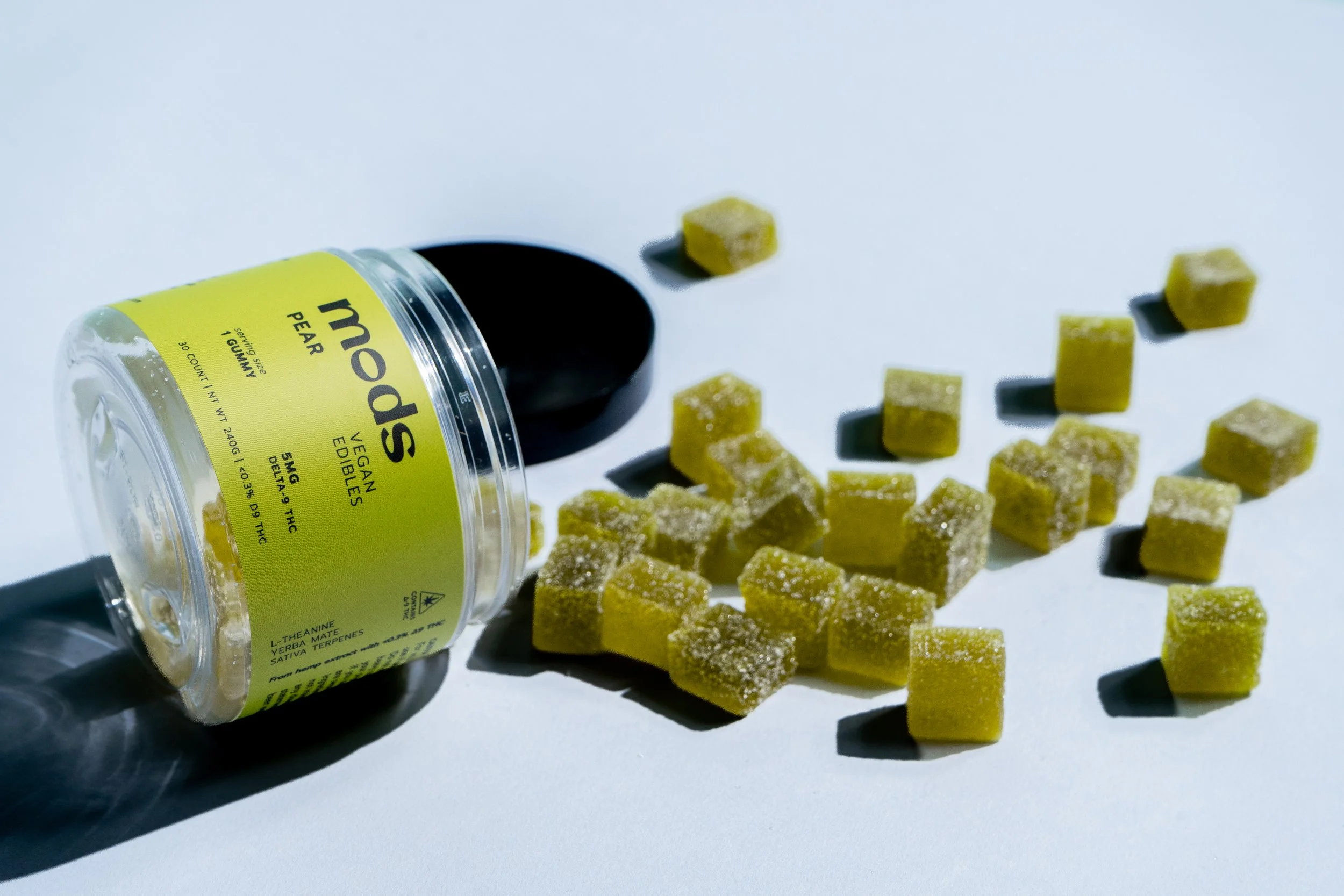 A container labeled 'mom PEAR', containing edible cannabis gummies, with some gummies spilled out onto a white surface.