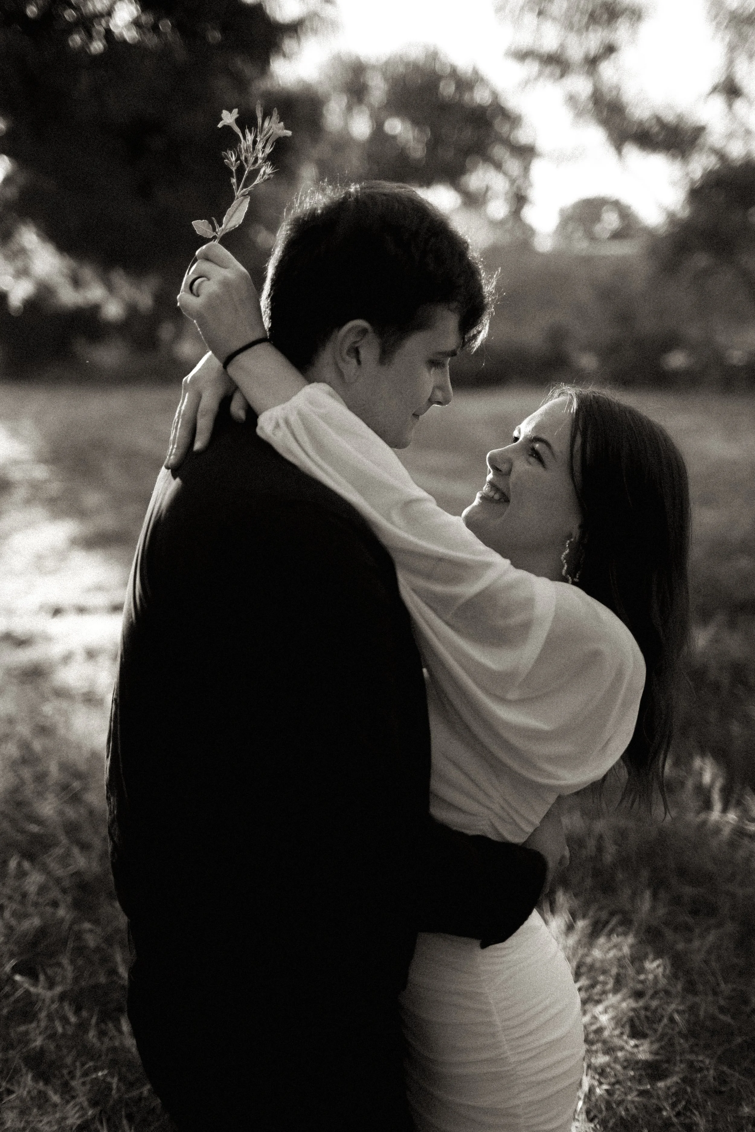 A couple embracing outdoors, smiling and looking at each other, black and white photo
