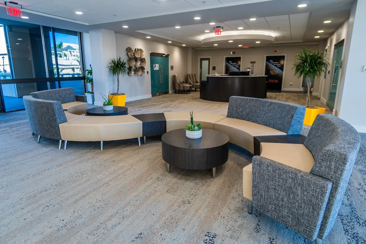 Picture of an office with a couch and table. Reception desk is featured in the background.