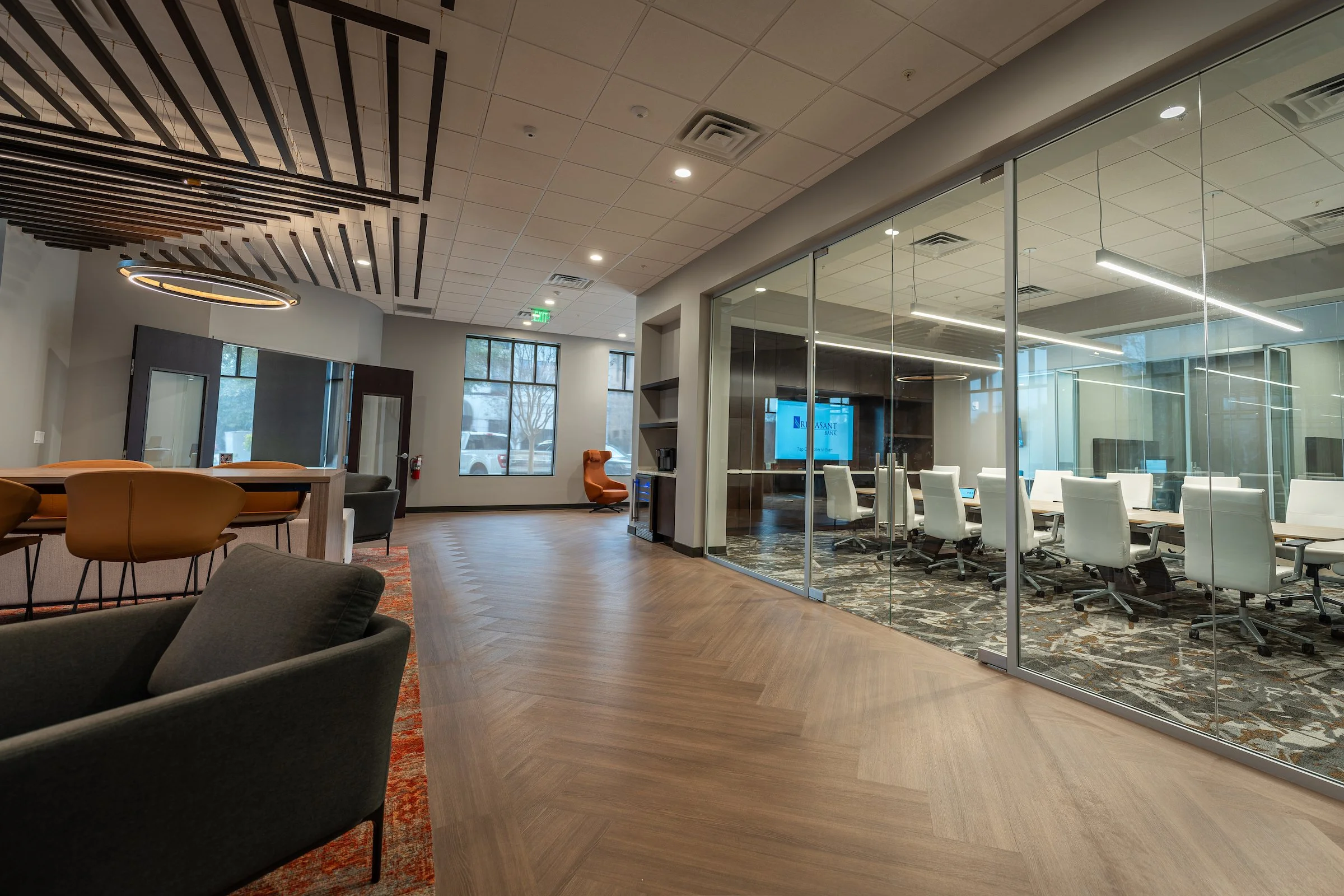 Modern office with herringbone flooring, glass-walled conference room, lounge seating, and a slatted ceiling feature.