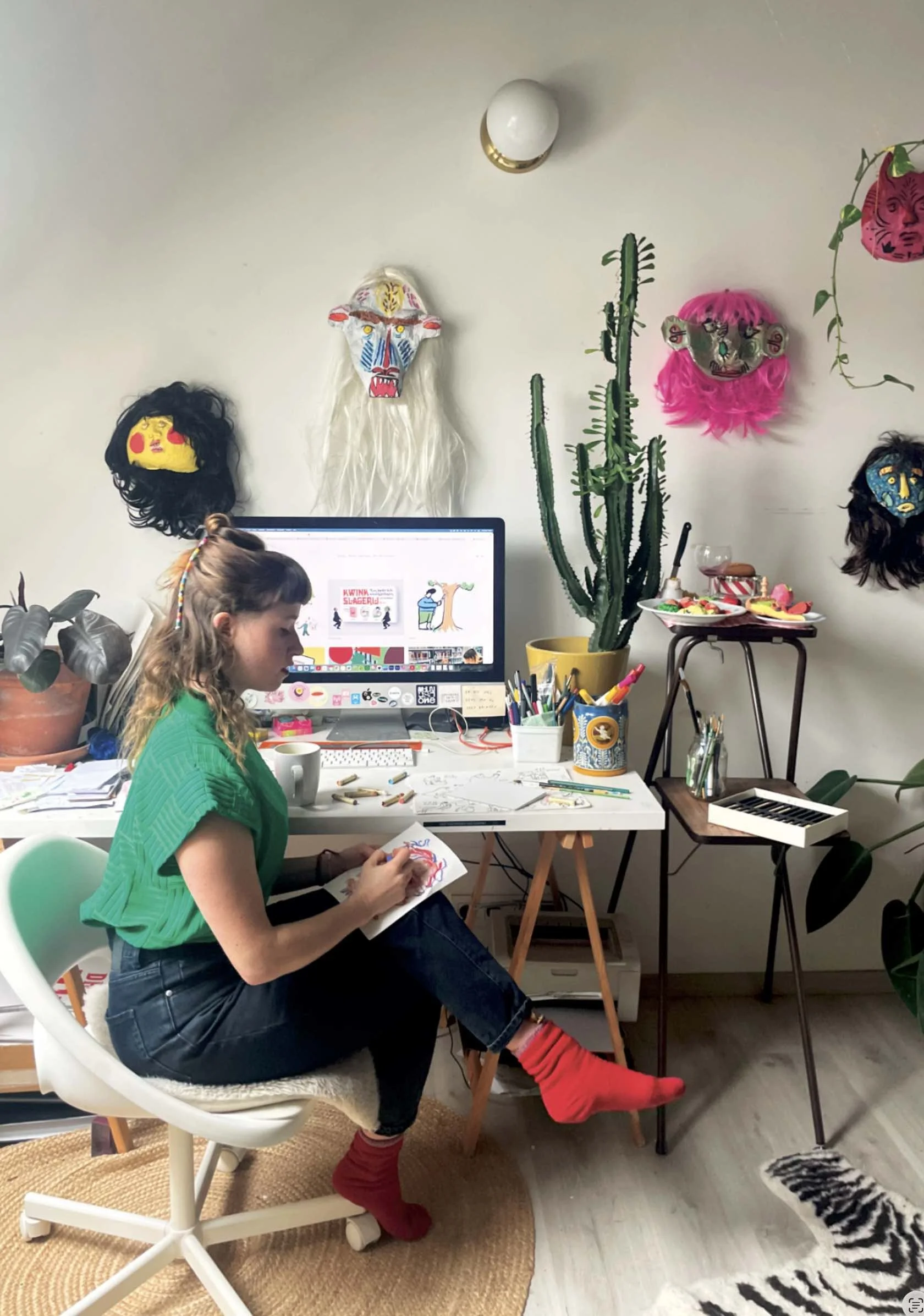 foto van Iris Van Robays achter haar bureau met maskers en een iMac op de achtergrond