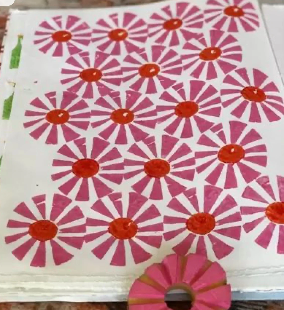 Sheet of pink and white circular flower-shaped stickers with red centers on a white background, with a few partially peeled or removed stickers and a pink and gold fan at the bottom.