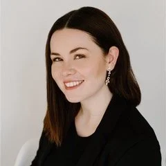 A woman with dark hair smiling, wearing earrings and a dark top, in black and white