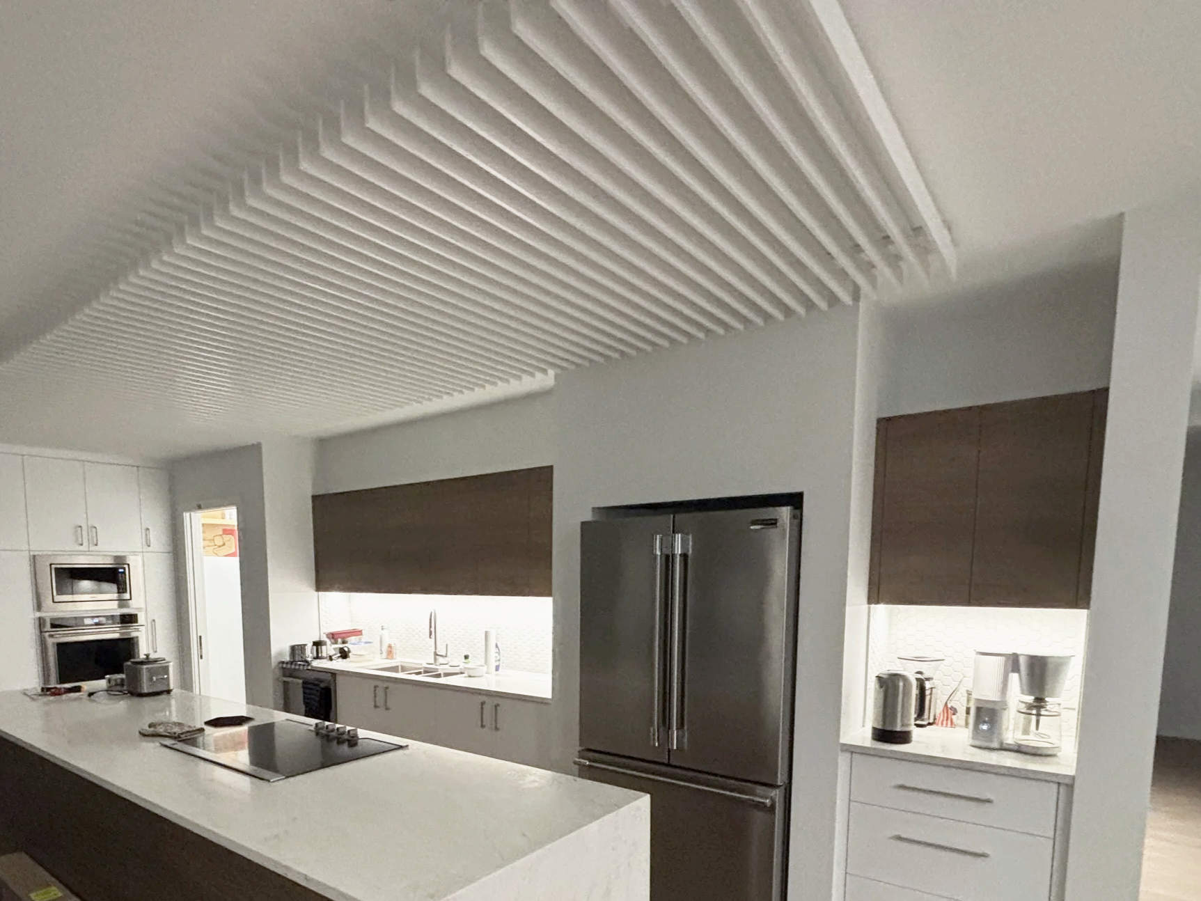 Modern kitchen with white island, stainless steel refrigerator, built-in microwave and oven, dark cabinets, and white backsplash with hexagonal tiles.