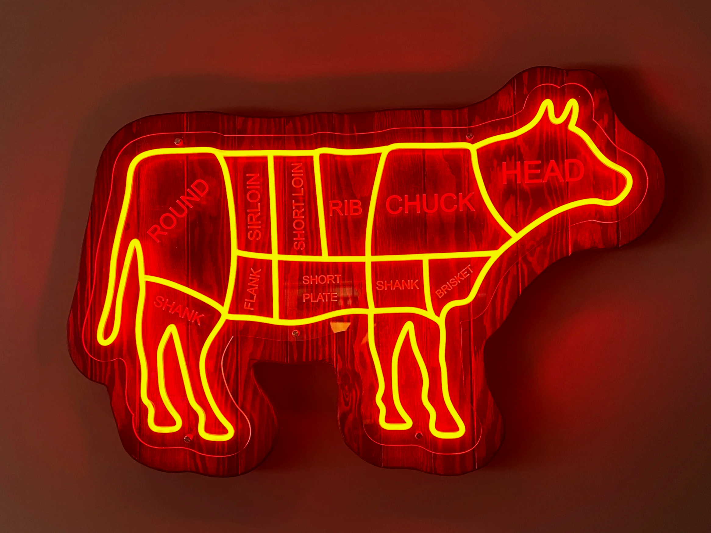 Neon sign in the shape of a cow, with sections labeled for various cuts of beef, including head, rib, chuck, short loin, sirloin, round, flank, shank, short plate, shank, brisket, and short loin.