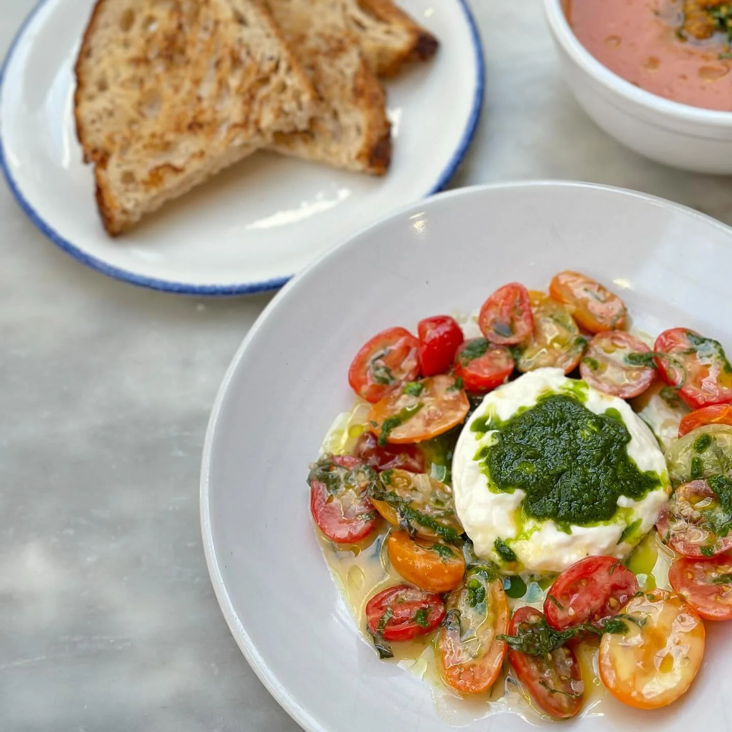 Summer cafe favorite! Tomatoes + Burrata - layered with marinated heirloom tomatoes, burrata cheese, olive oil, basil pesto (nut free), served with griddled country bread. 🍞 🍅