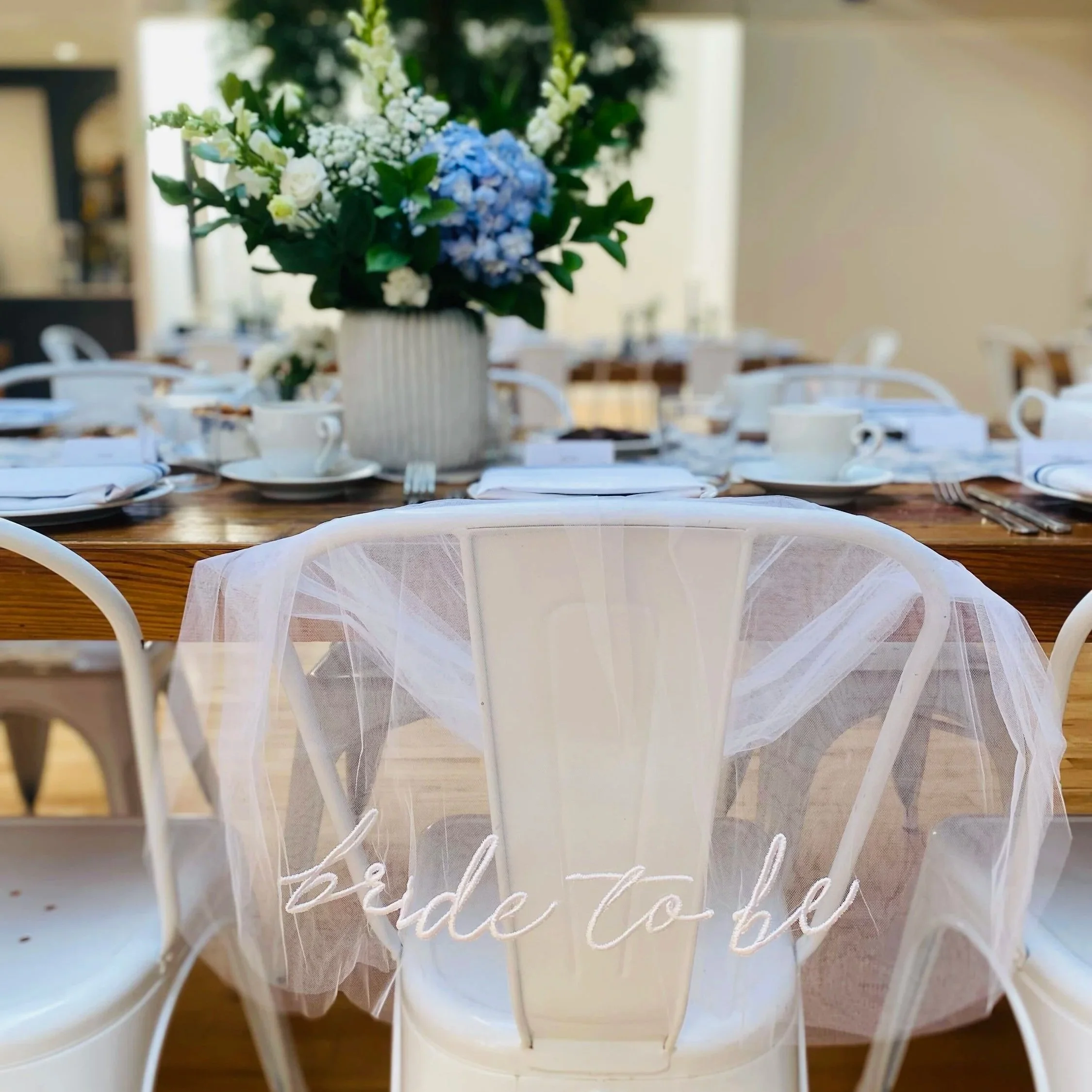 A floral centerpiece with white and blue flowers on a table set for dining, with a white cloth runner underneath.