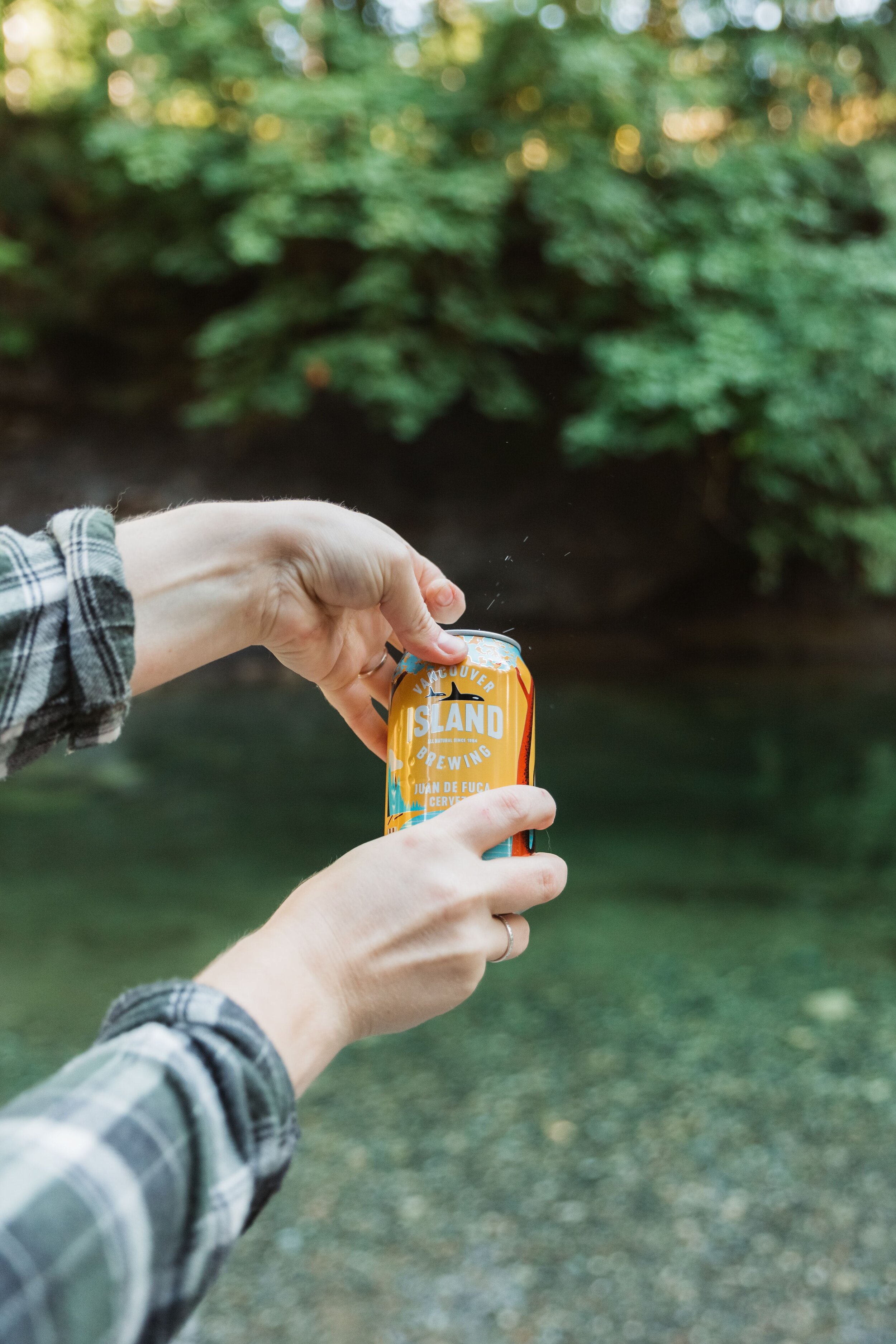 Person opening a can of Vancouver Island Brewing beer outdoors.