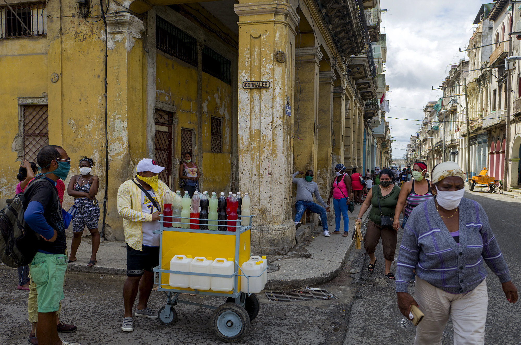  Cubanos caminan en bsqueda de comida mientras un vendedor de refresco espera por compradores.  